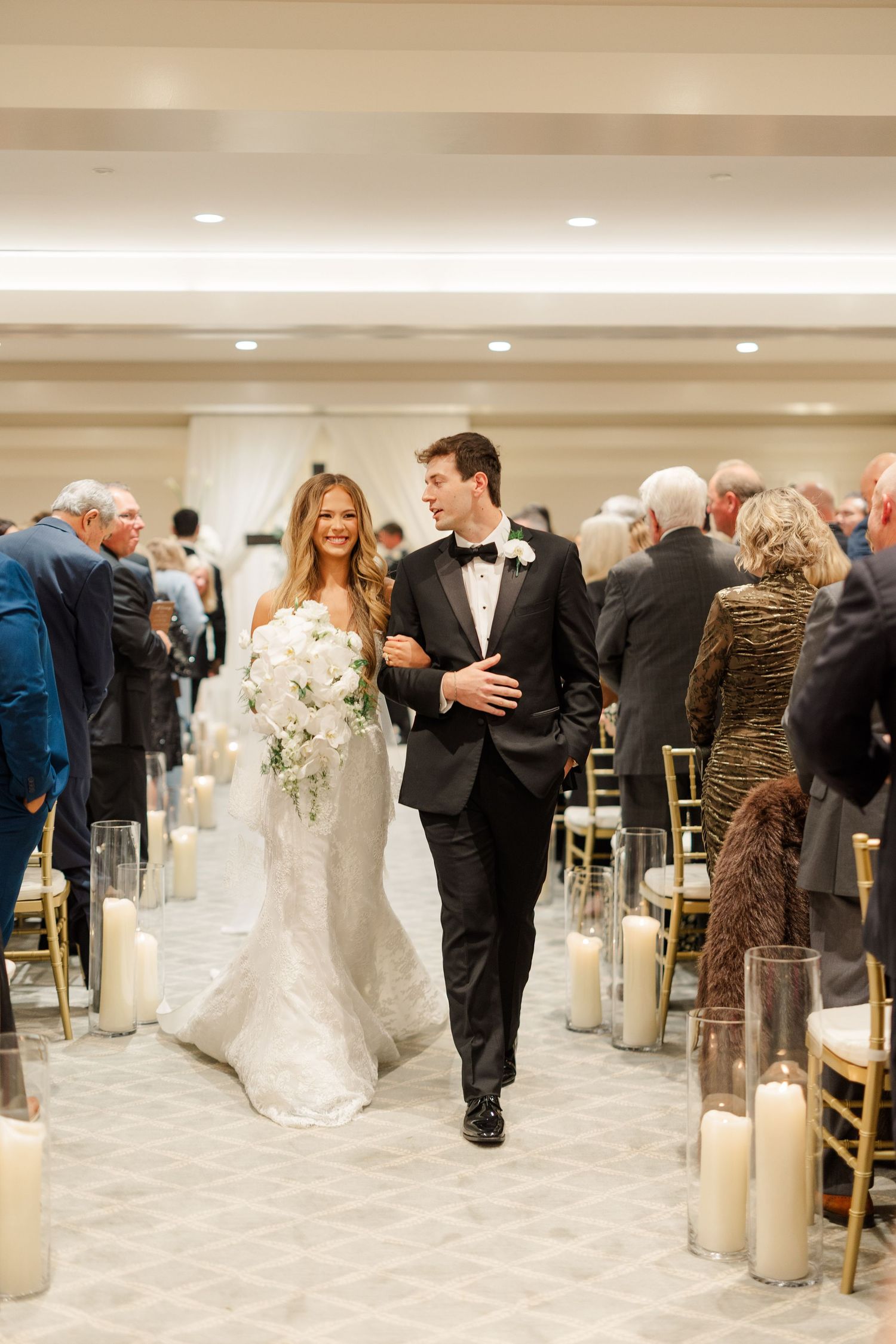 A wedding ceremony recessional with candle-lined aisle in an elegant ballroom setting.