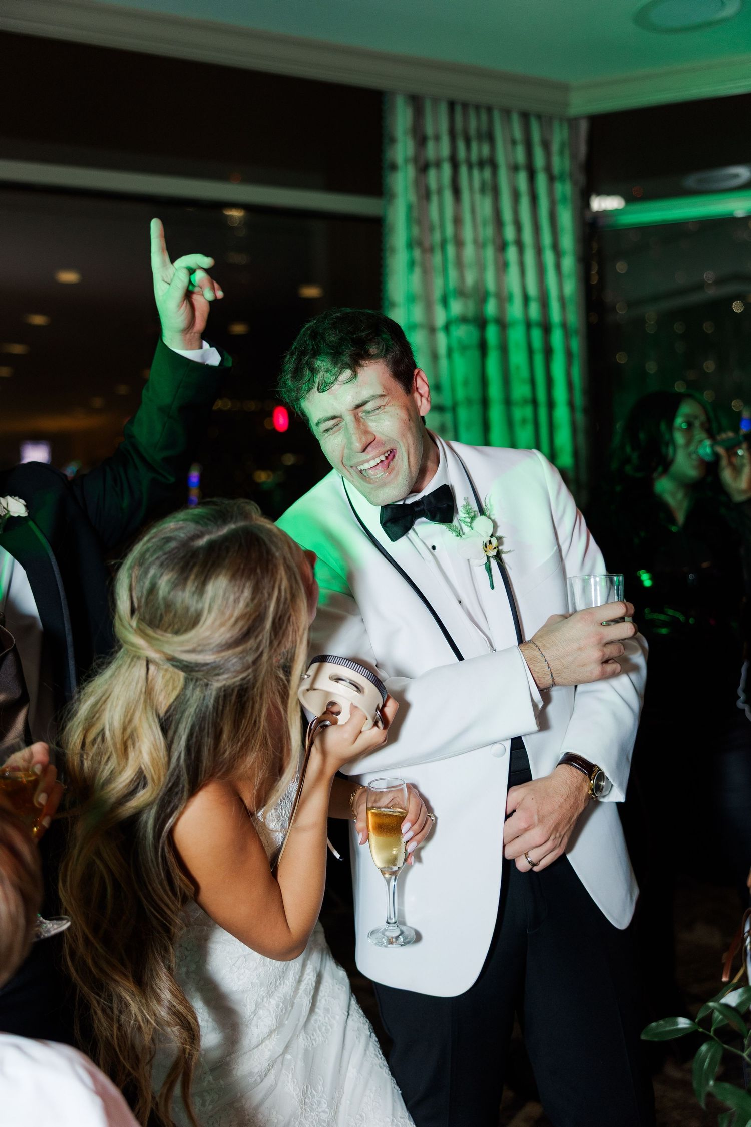 Wedding celebration with guests dancing and enjoying champagne under green lighting.