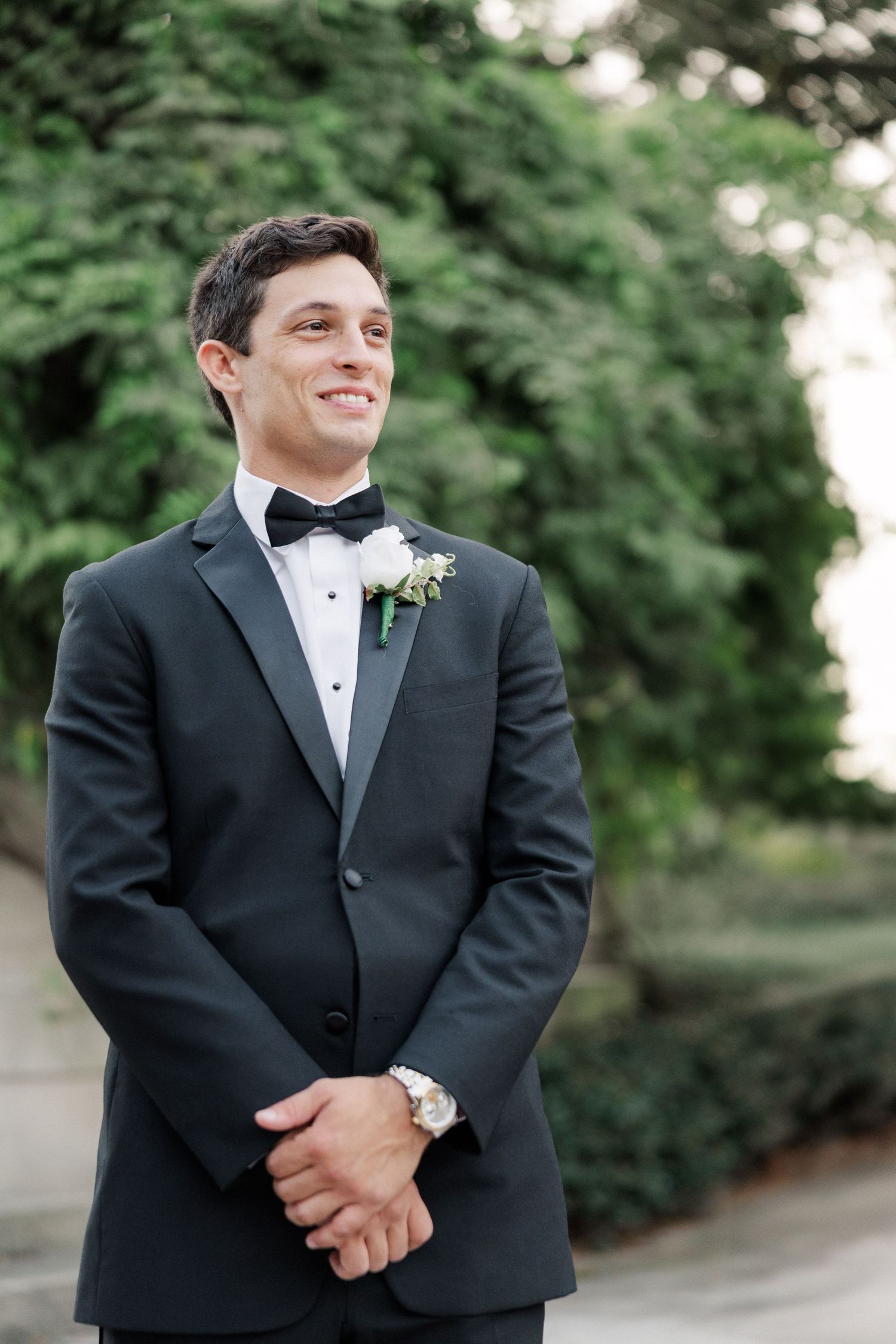 Groom in classic black tuxedo and bow tie smiles during outdoor wedding portraits.