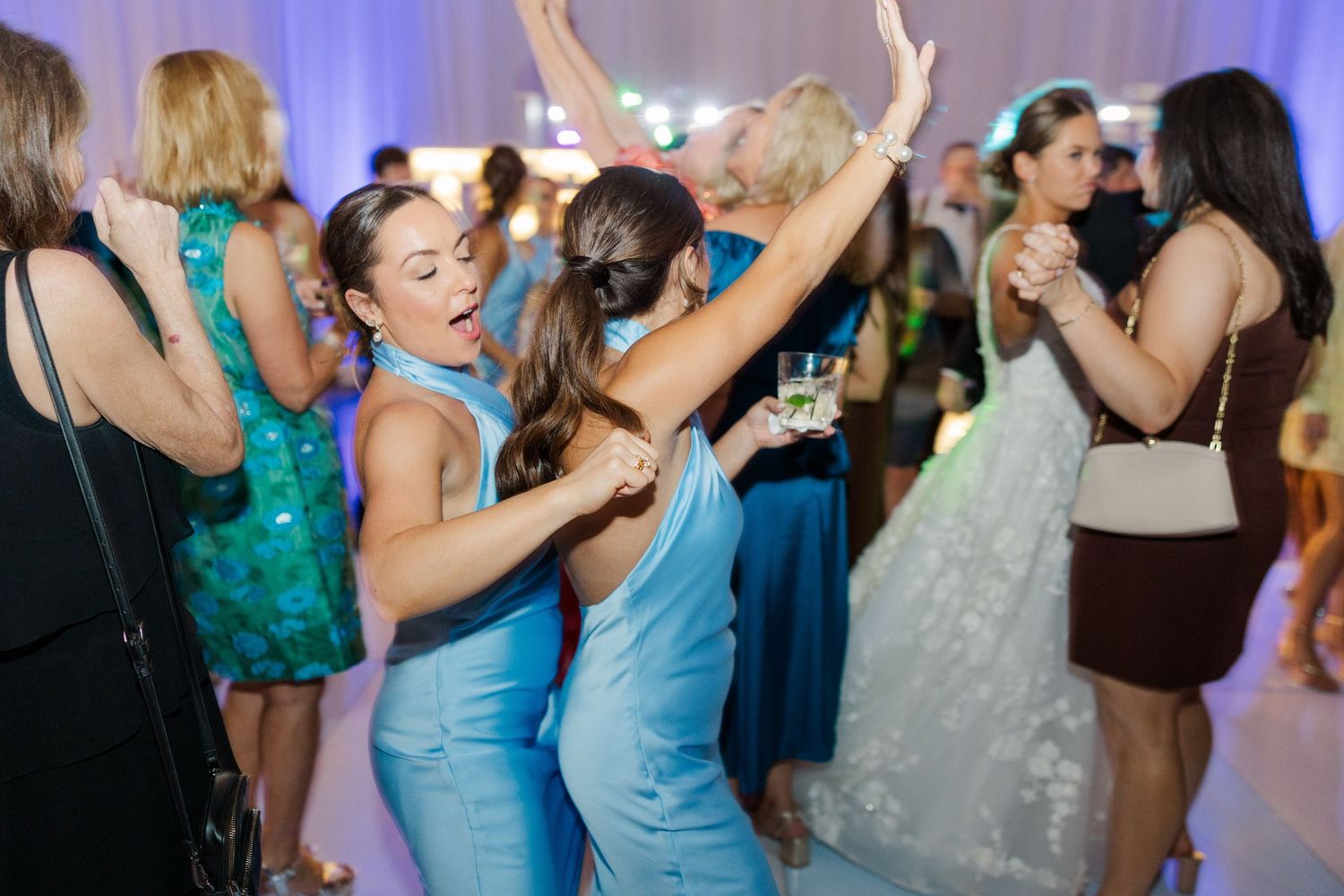 Wedding guests dancing and celebrating at reception with blue and teal dresses.