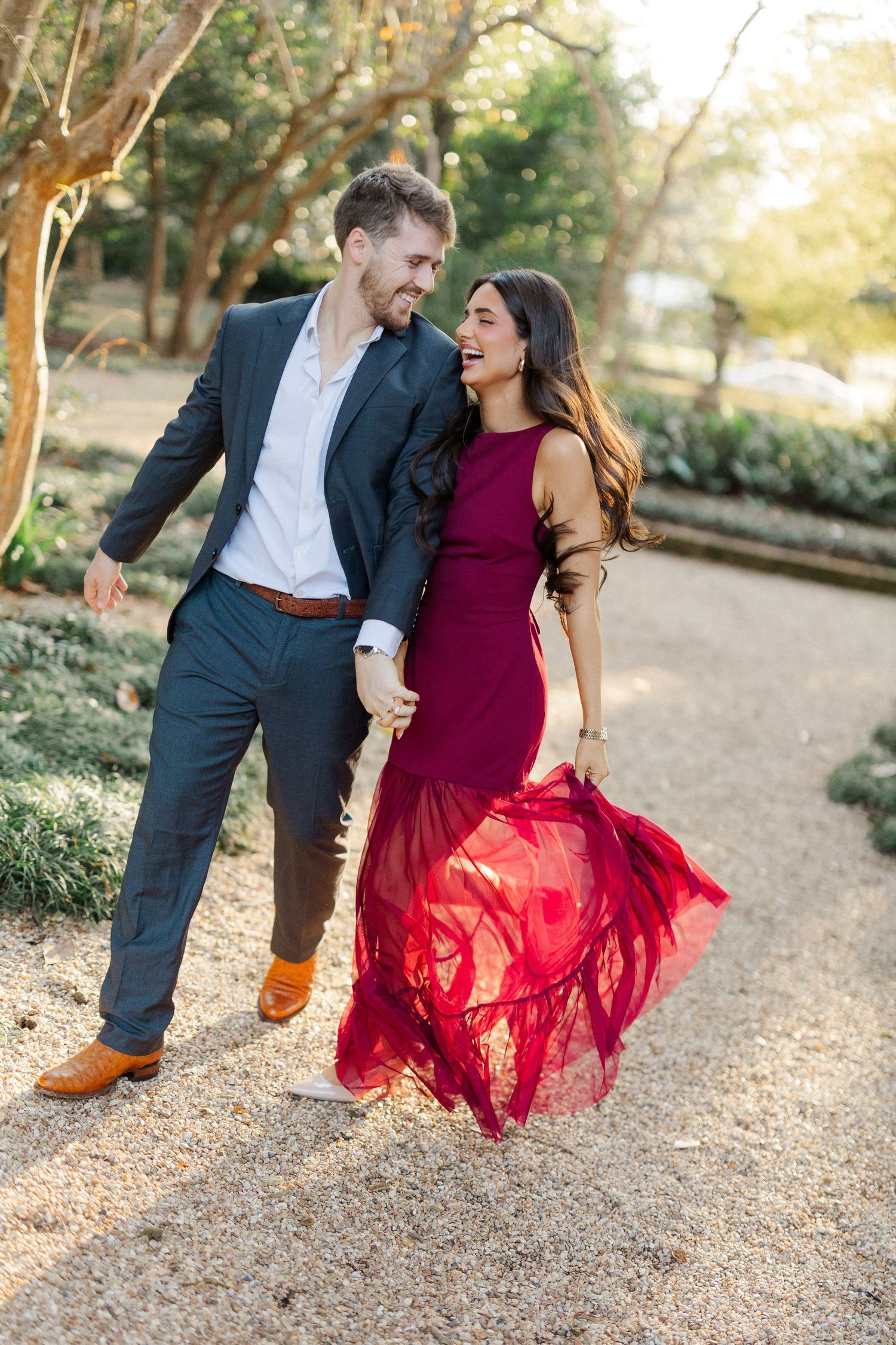 A couple shares a joyful moment dancing together outdoors, with her burgundy dress flowing in the motion.