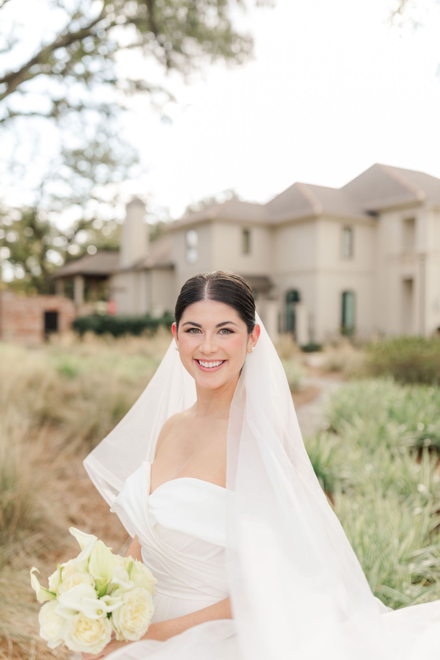 A radiant bride in a strapless gown holds a cream bouquet while her veil flows in the breeze.