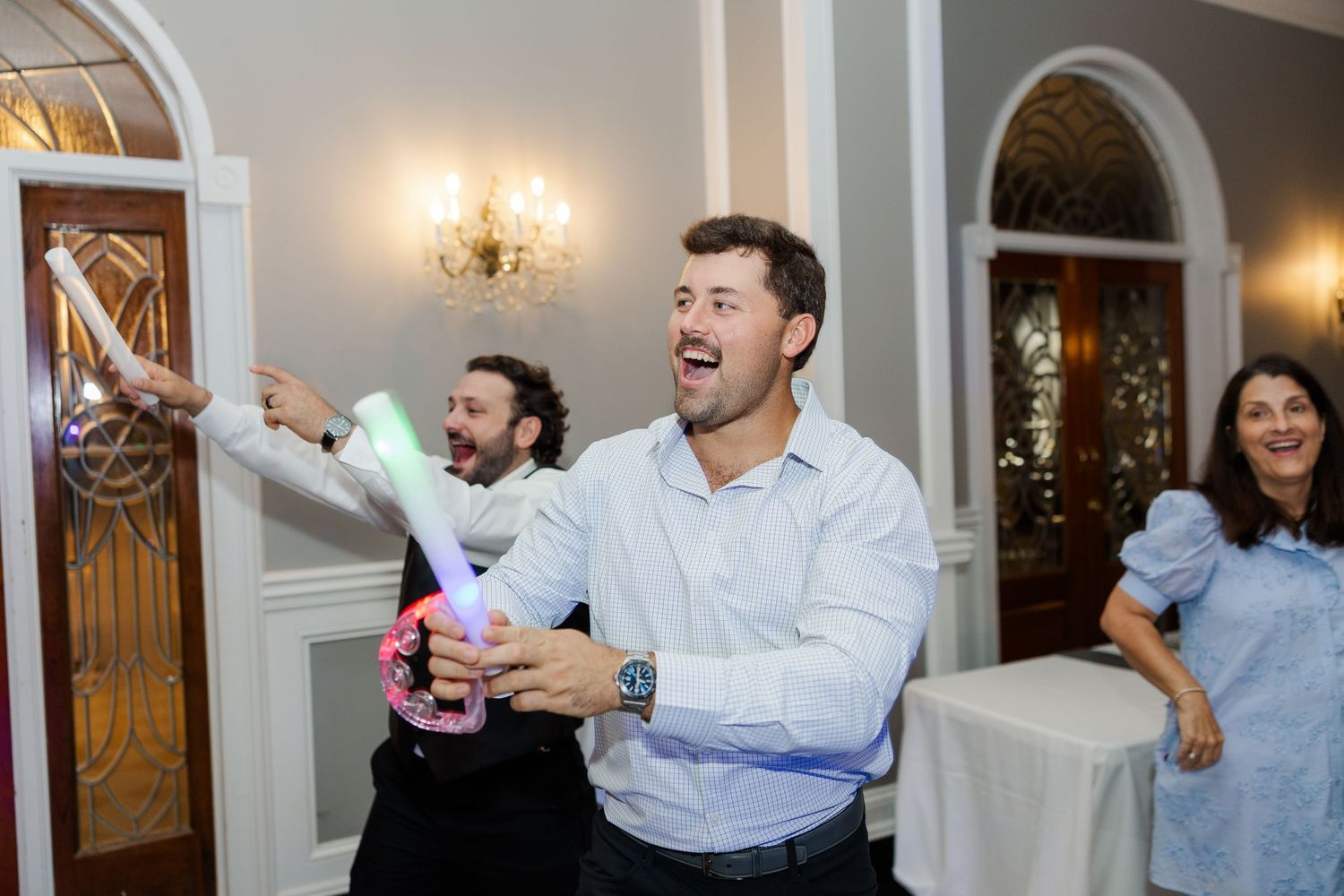 Wedding guests laugh and celebrate during a joyful reception moment in an elegant indoor venue.