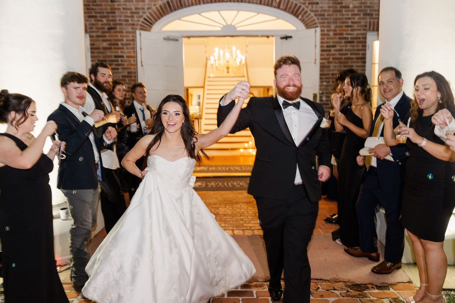 Newlyweds make their grand exit through a brick archway while guests cheer with sparklers.
