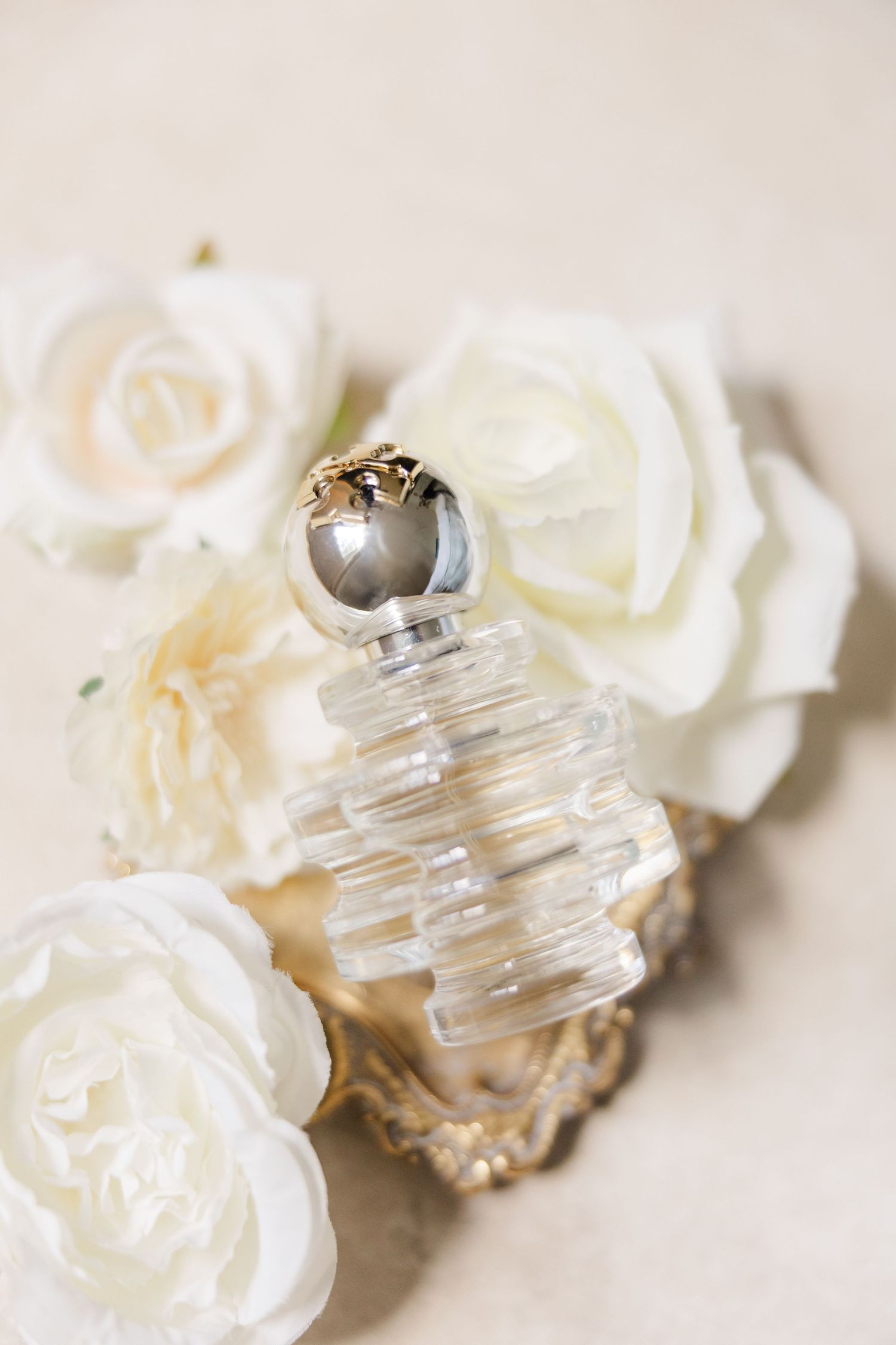 White roses and crystal perfume bottle arranged on light surface for elegant wedding detail photography.