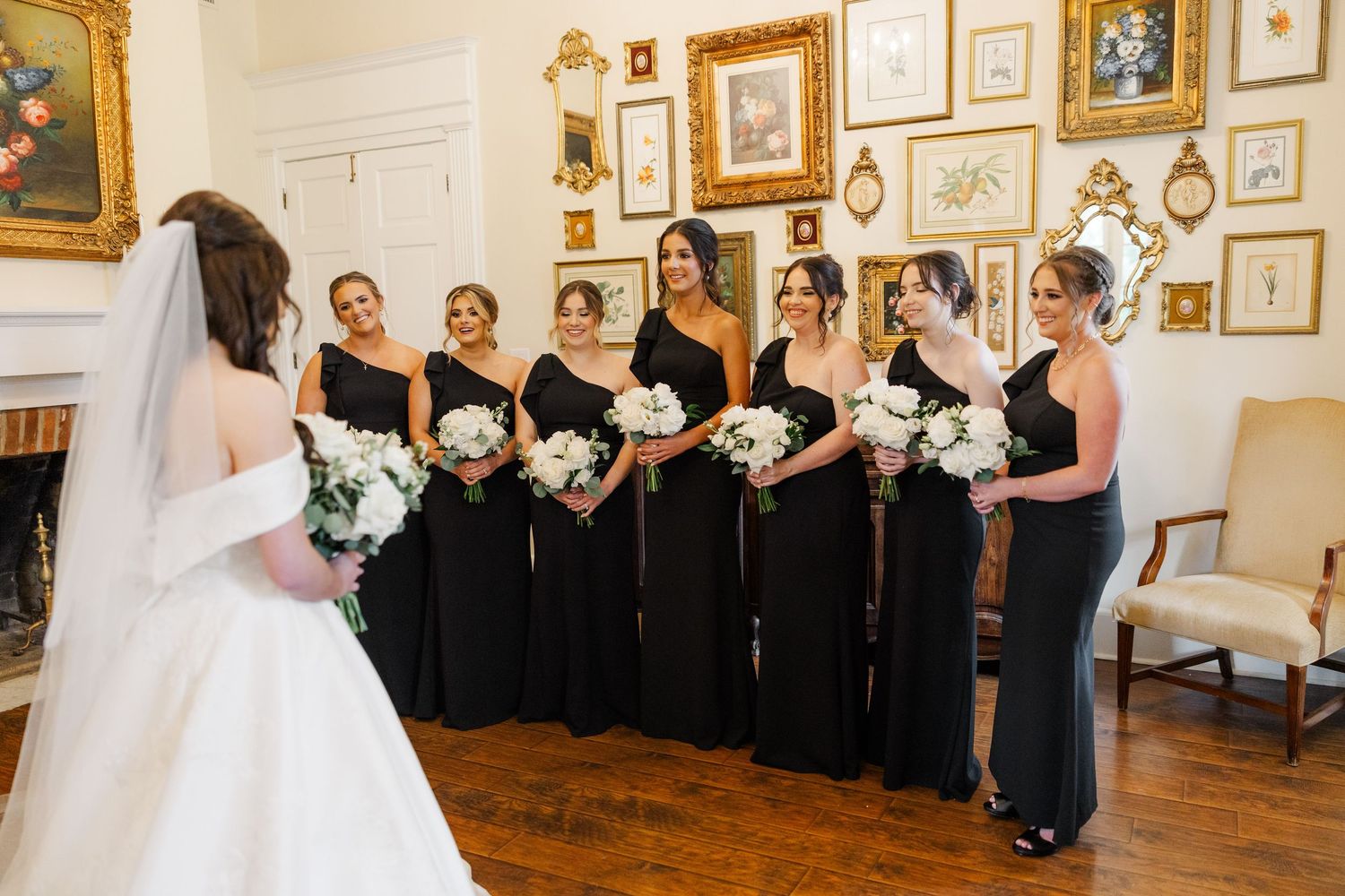 Wedding party lined up in formal attire against a wall decorated with framed artwork.