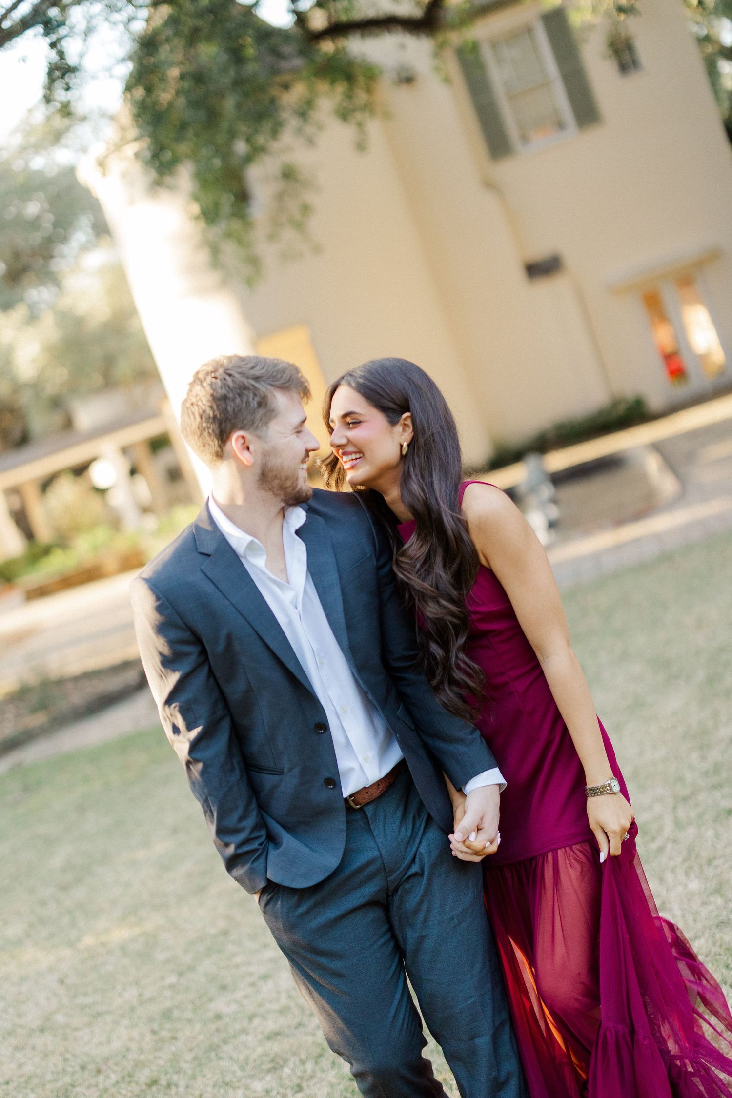 Romantic couple in burgundy dress and navy suit sharing intimate moments outdoors.