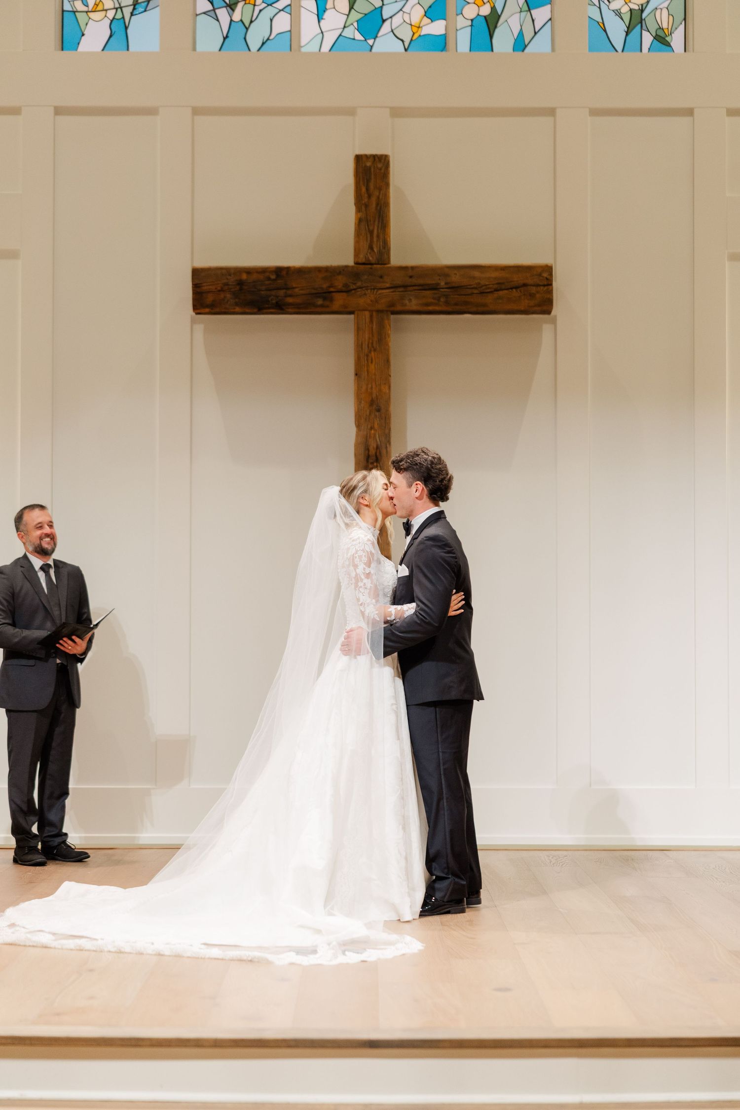 Wedding ceremony in a modern church with stained glass windows and wooden cross on stage.