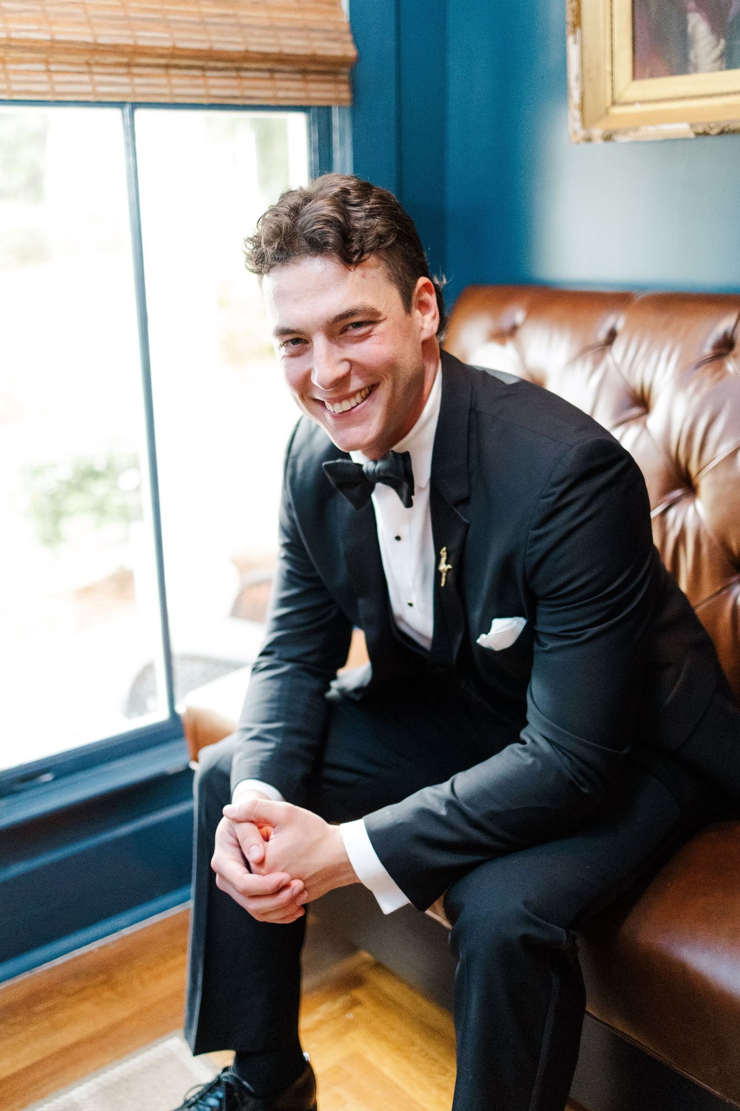 A person in a black tuxedo sits on a leather bench by a window, shown in a series of candid poses.