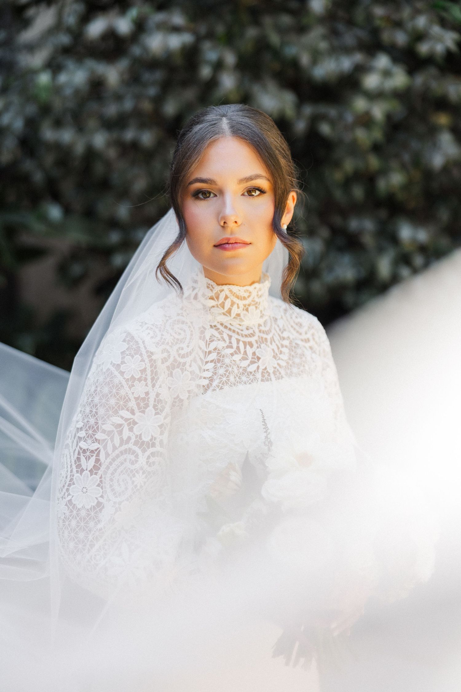 An ethereal bridal portrait features soft lighting and delicate lace details through a flowing white veil.