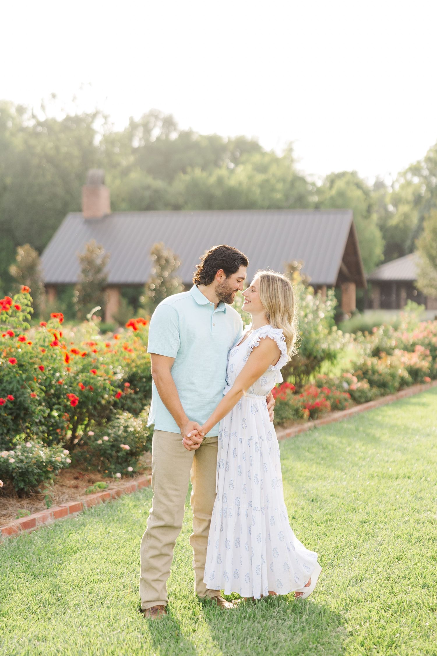 A couple shares a romantic moment together in a garden with blooming roses during golden hour.