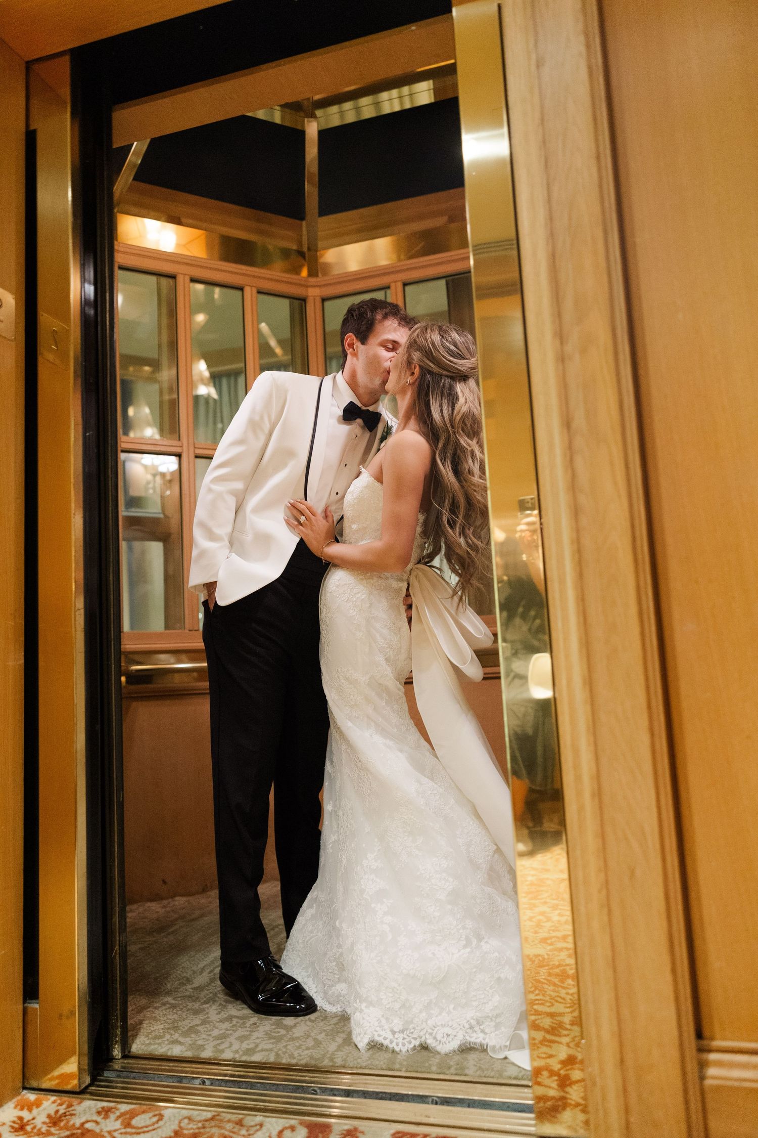 Wedding couple shares intimate moments in mirrored hallway with warm lighting.