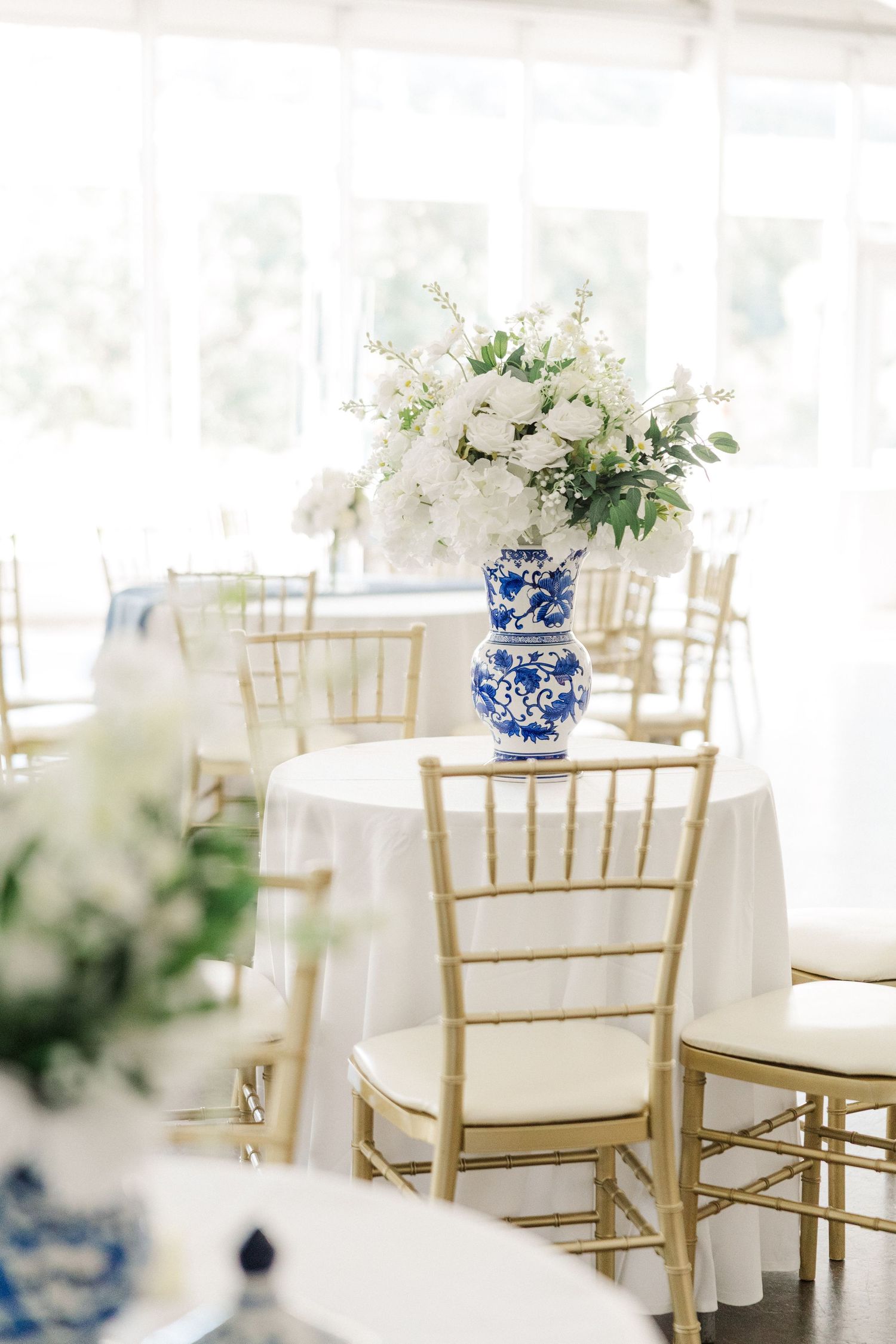Elegant wedding reception setup with gold chiavari chairs and blue and white floral centerpieces.