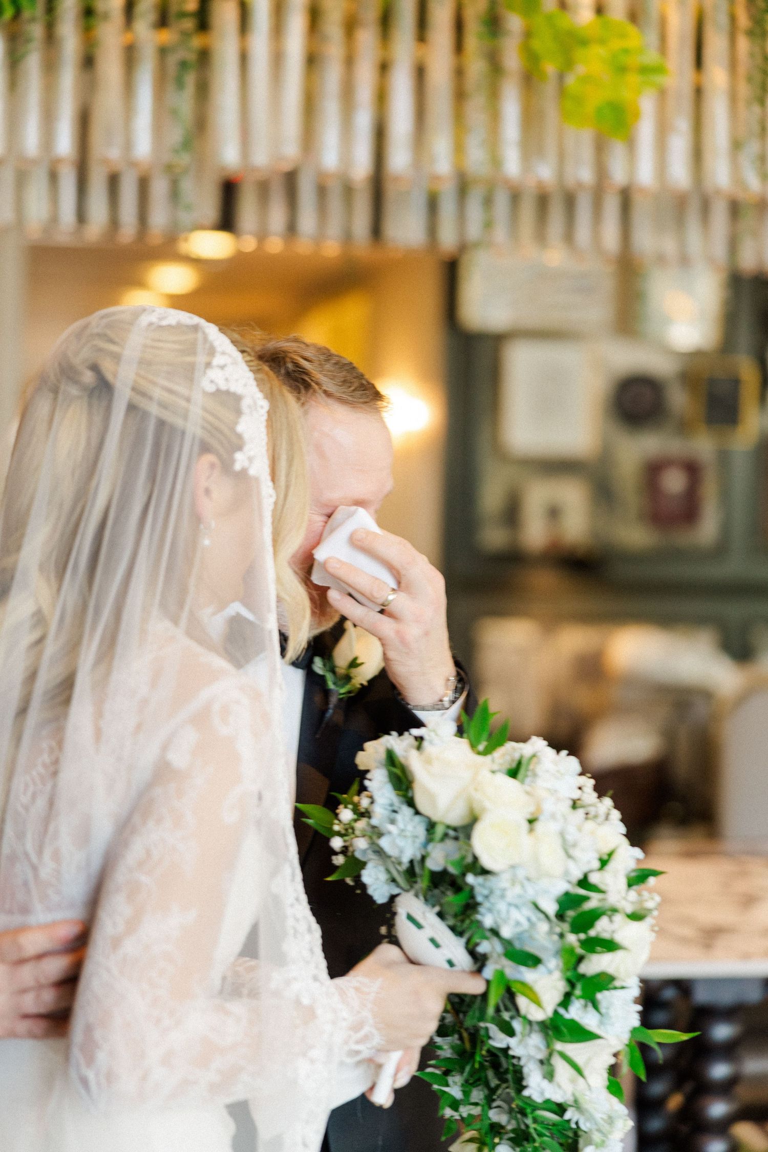 Side view of couple sharing emotional first look moment with white roses and veil.