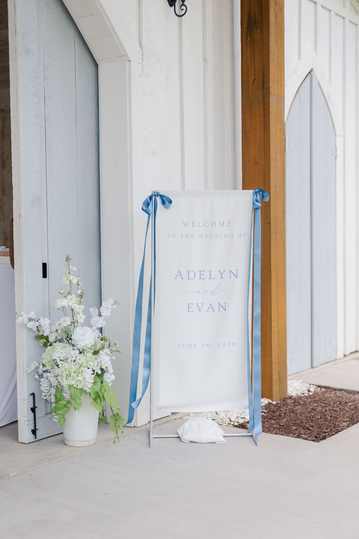 Wedding welcome sign for Adelyn and Evan with blue ribbon bows beside white floral arrangement at barn venue.
