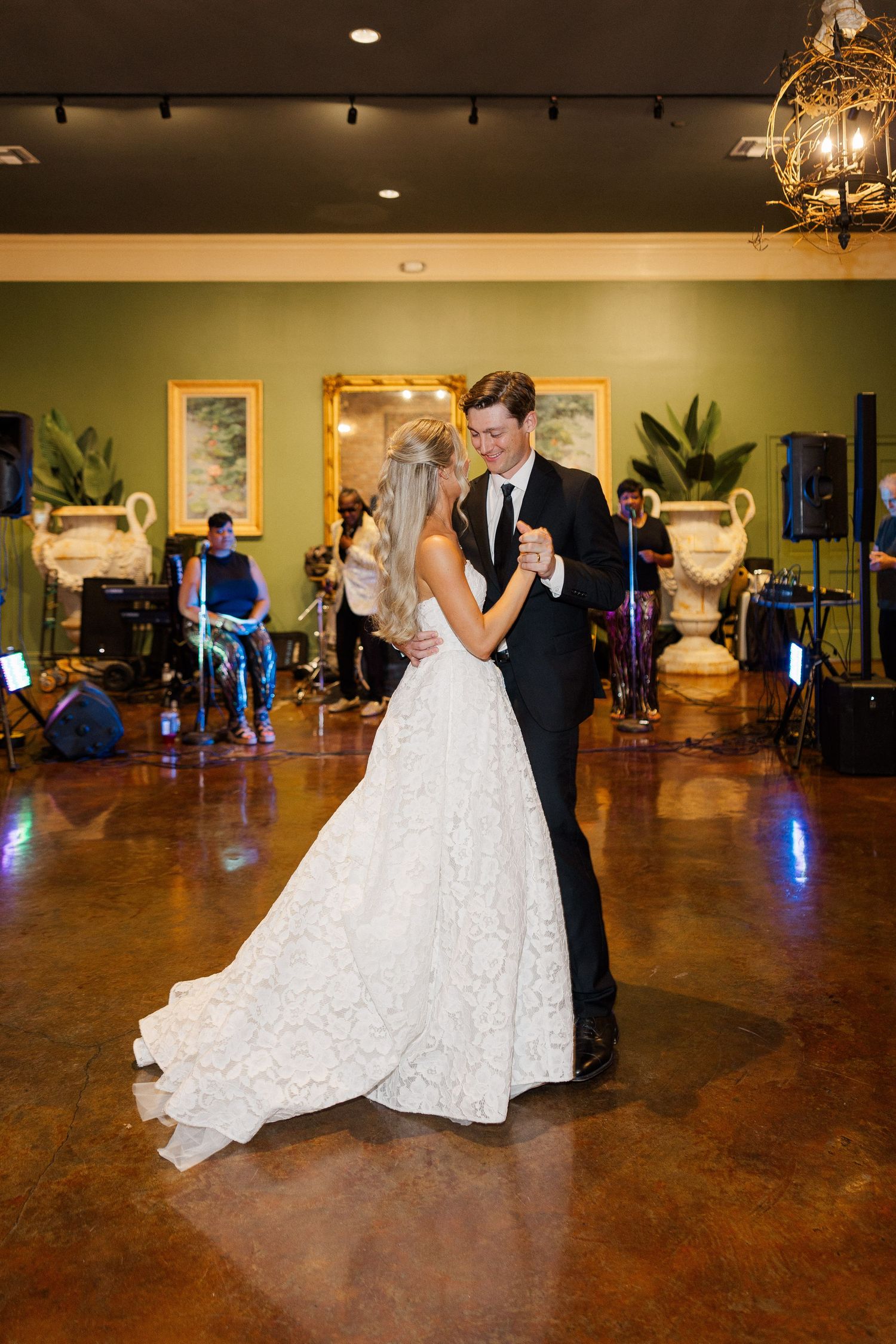 Bride and groom share their first dance on a polished floor with a live band performing in the background.