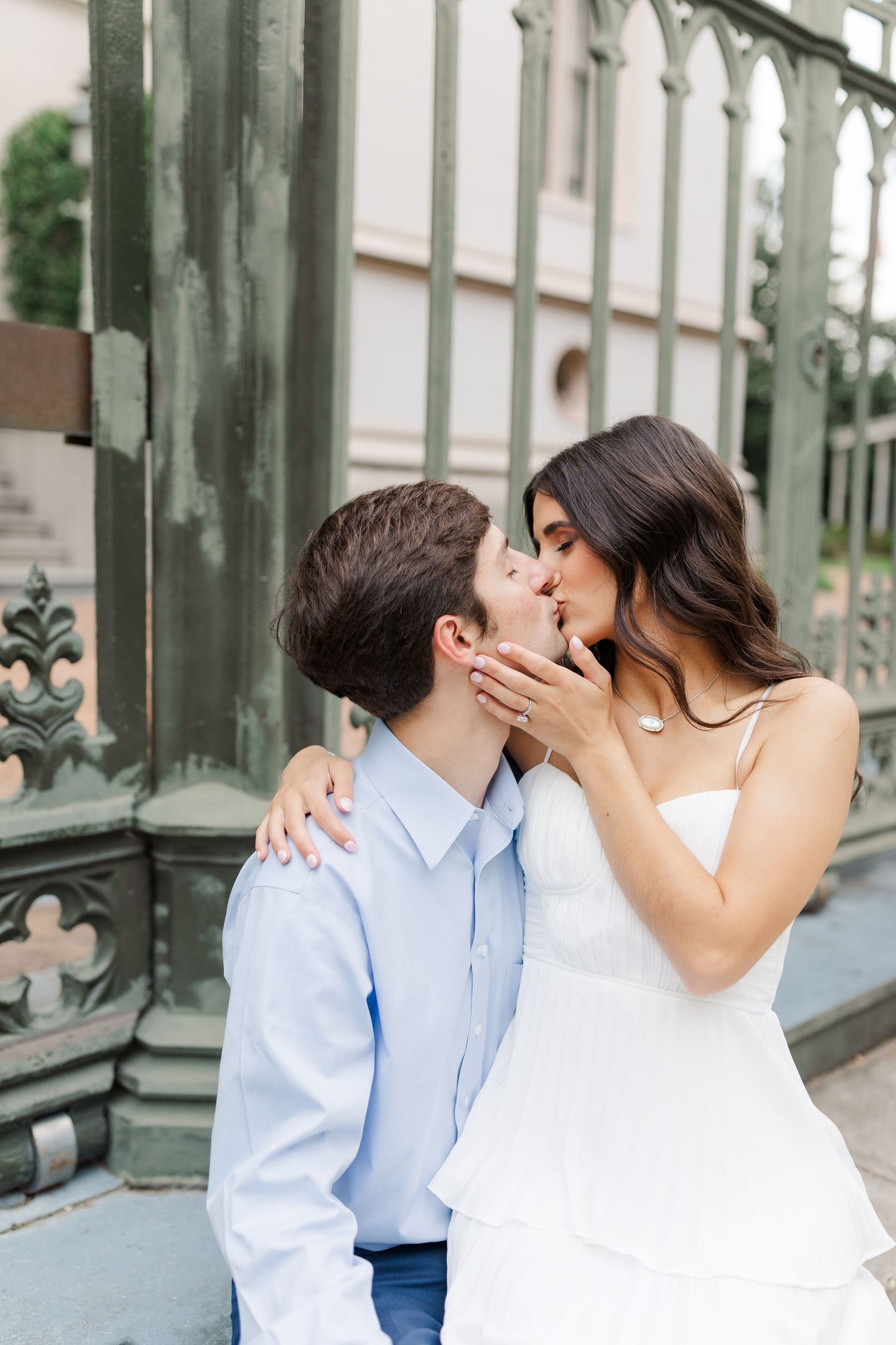 A romantic couple sharing a tender kiss outdoors near decorative wrought iron railings.