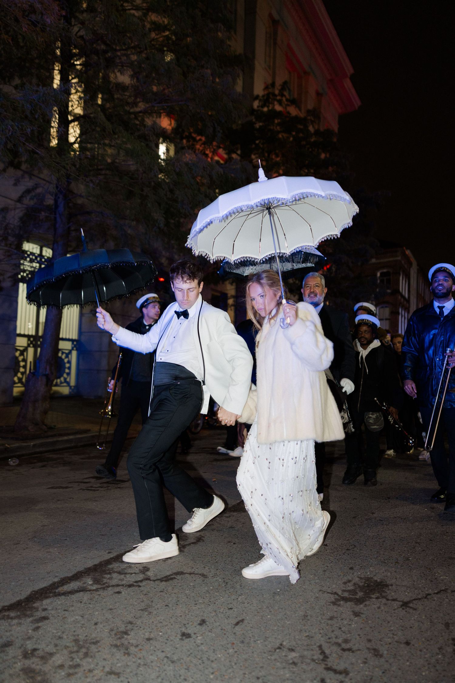 Wedding party dances with white umbrellas during nighttime outdoor celebration.