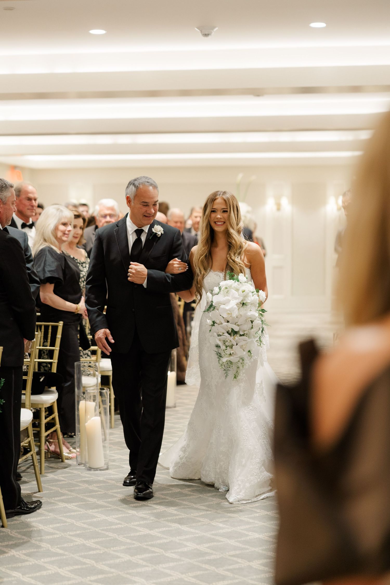 Wedding reception scene showing guests and bridal party walking through an elegant ballroom.
