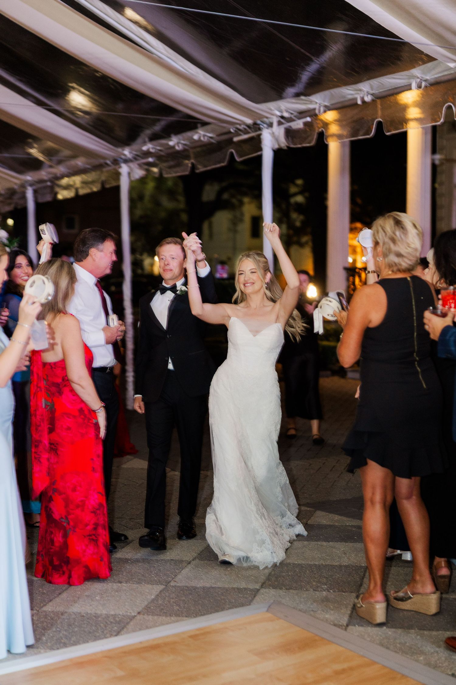 Wedding reception dance floor filled with guests celebrating under a clear tent structure at night.