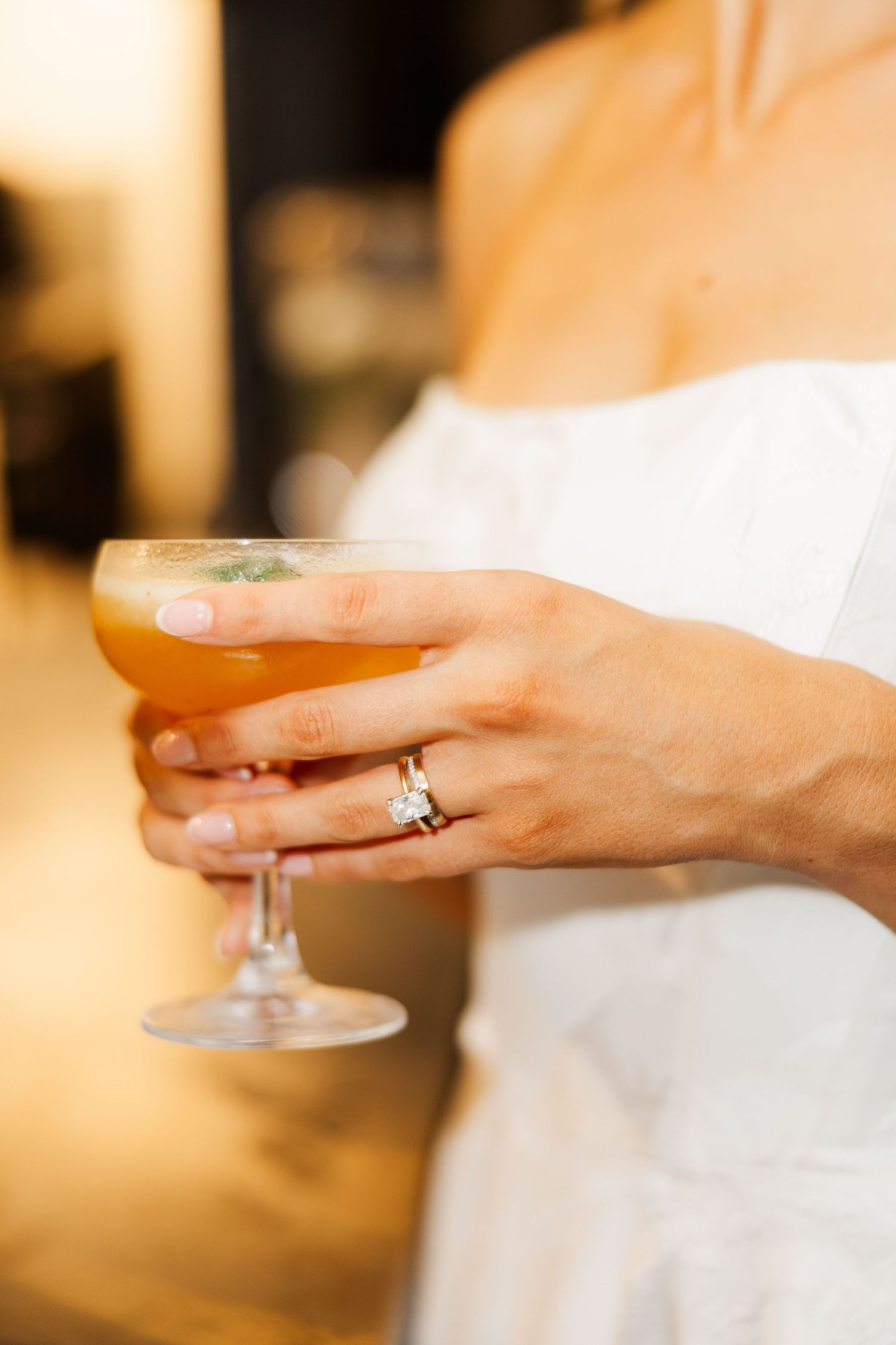 Close-up of hands holding a champagne glass, showing a wedding ring detail.
