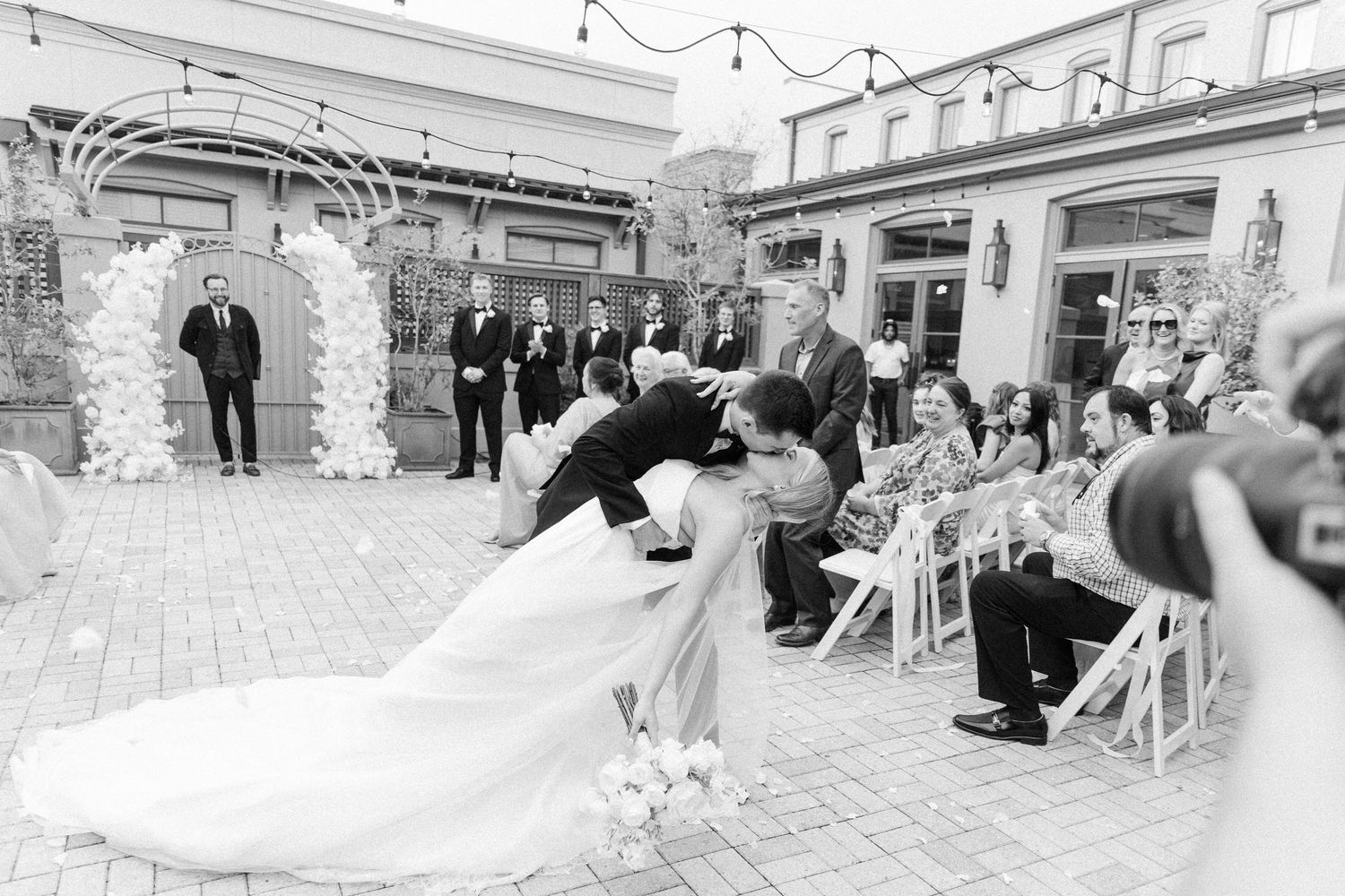 Wedding ceremony exit with guests lining the brick pathway under string lights.