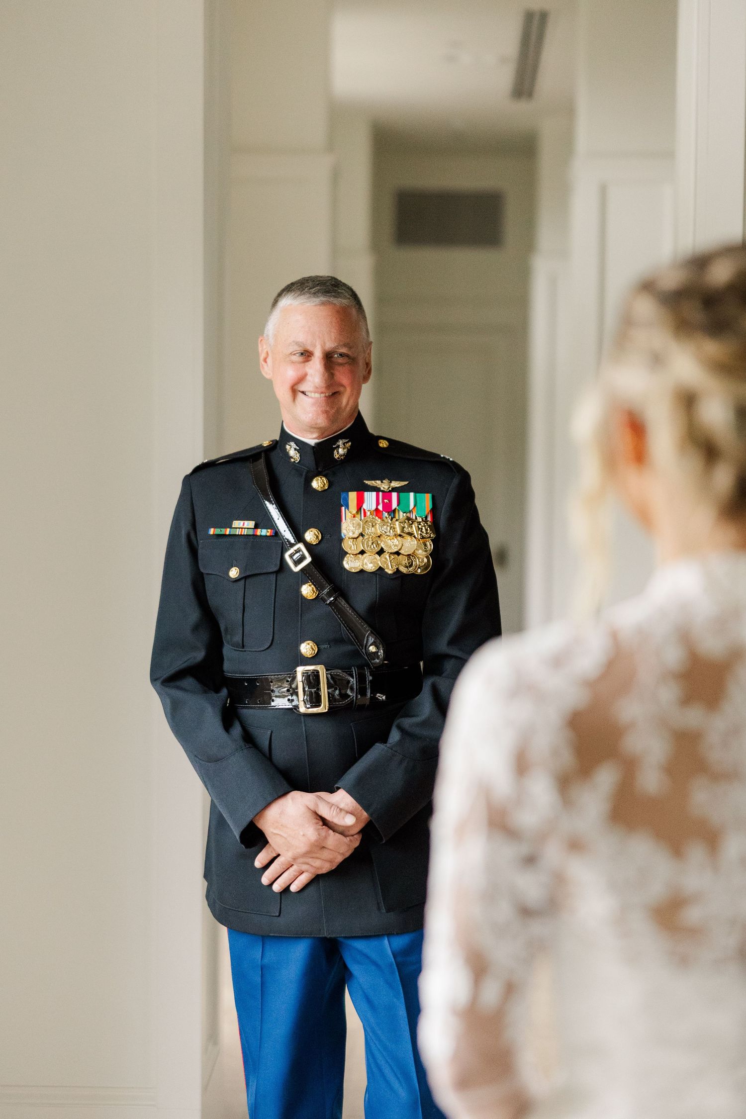Marine in dress blues and medals stands in anticipation before his bride in a white lace wedding dress.