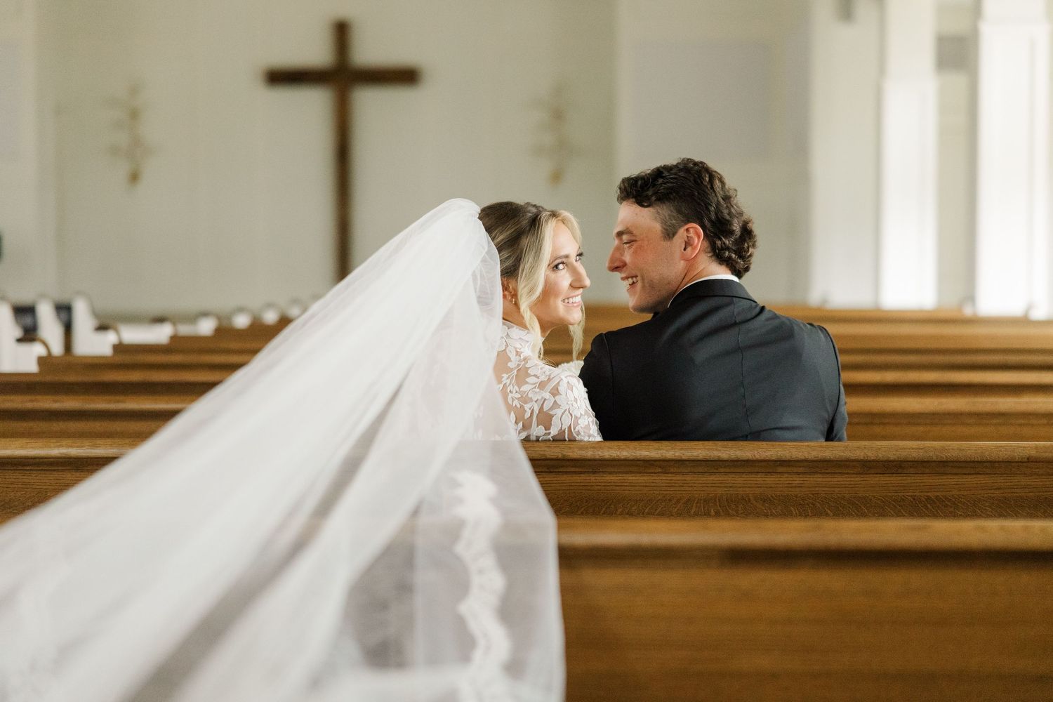 A tender moment between newlyweds seated in wooden church pews.