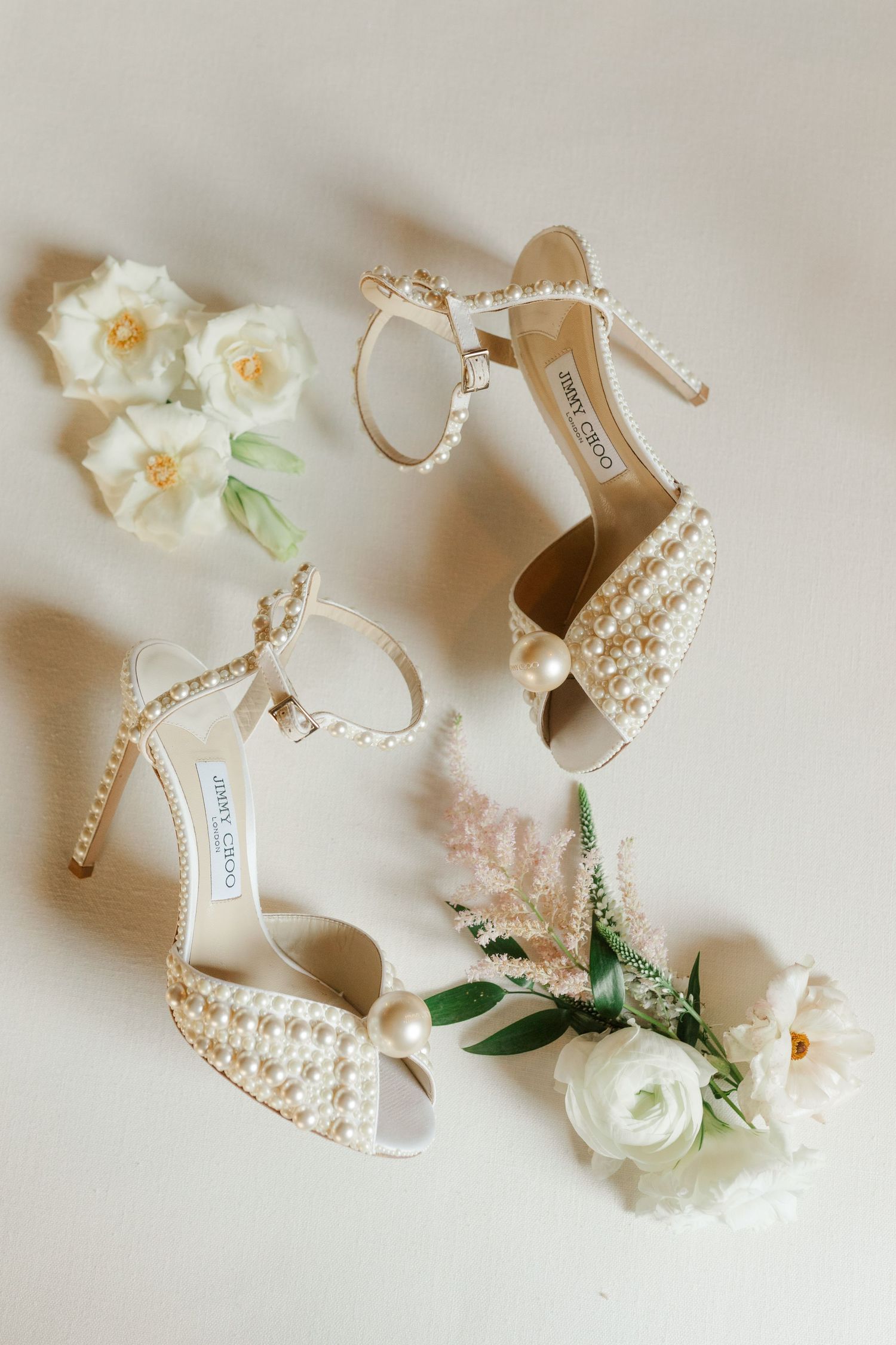 Pearl-embellished wedding heels with white floral accents on light background.