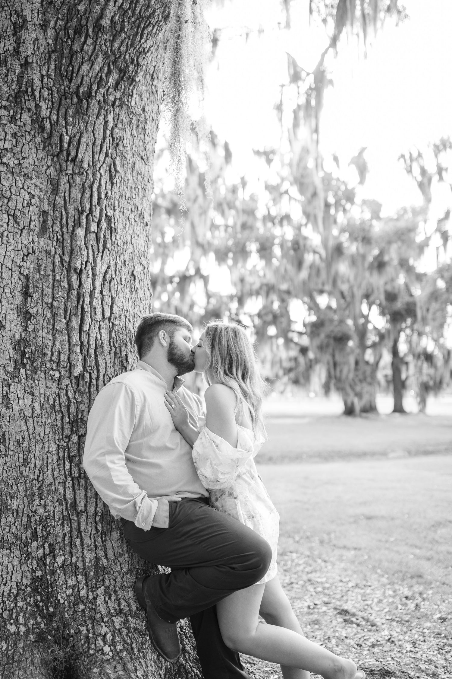 A romantic black and white portrait of a couple sharing an intimate moment against a large tree with spanish moss.