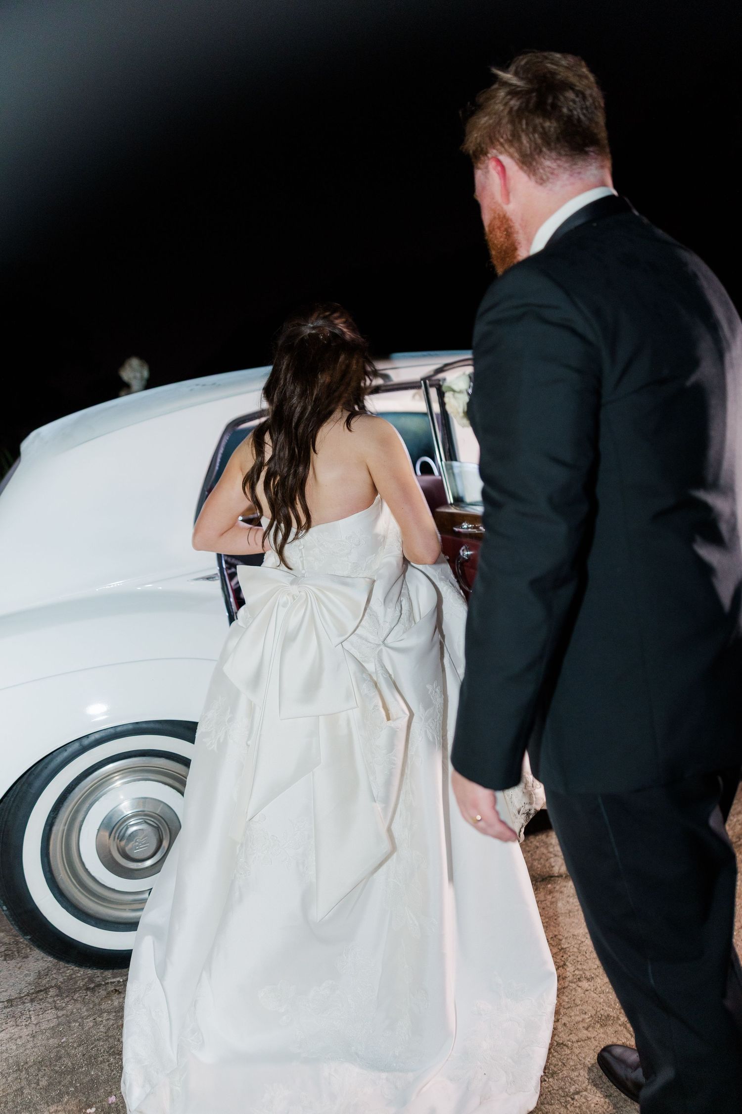 A close-up view of a bride's wedding dress train being arranged against a dark background.