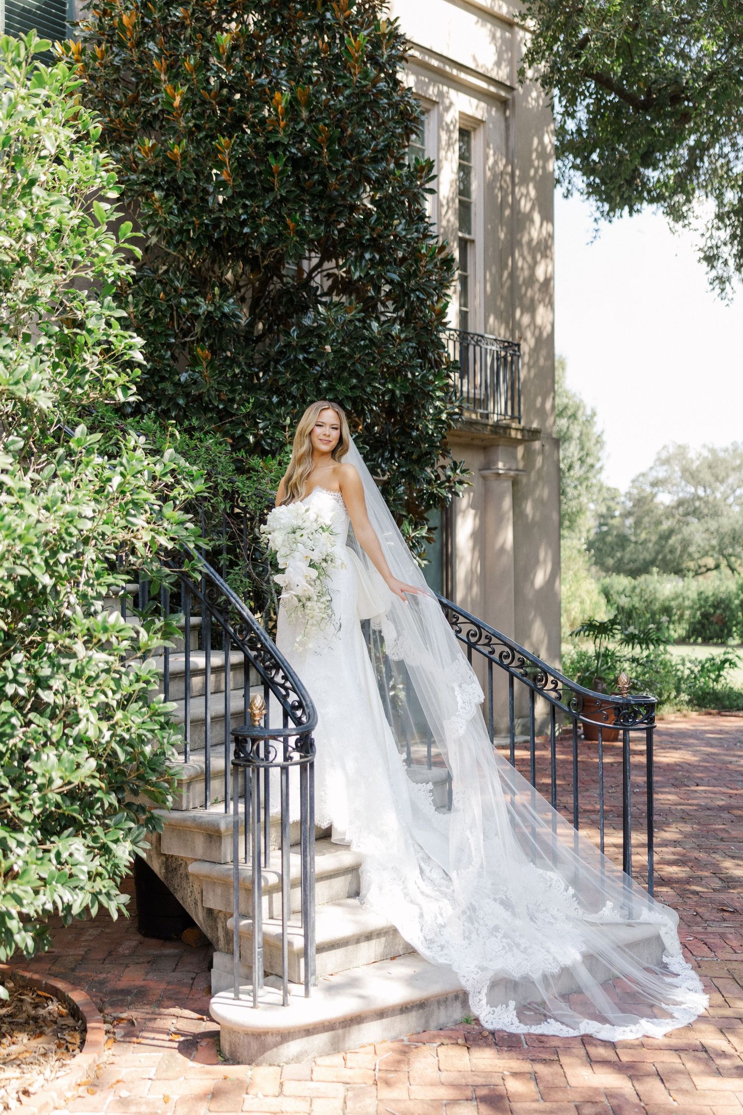 Dramatic bridal portrait on mansion steps with flowing veil cascading down iron railings.