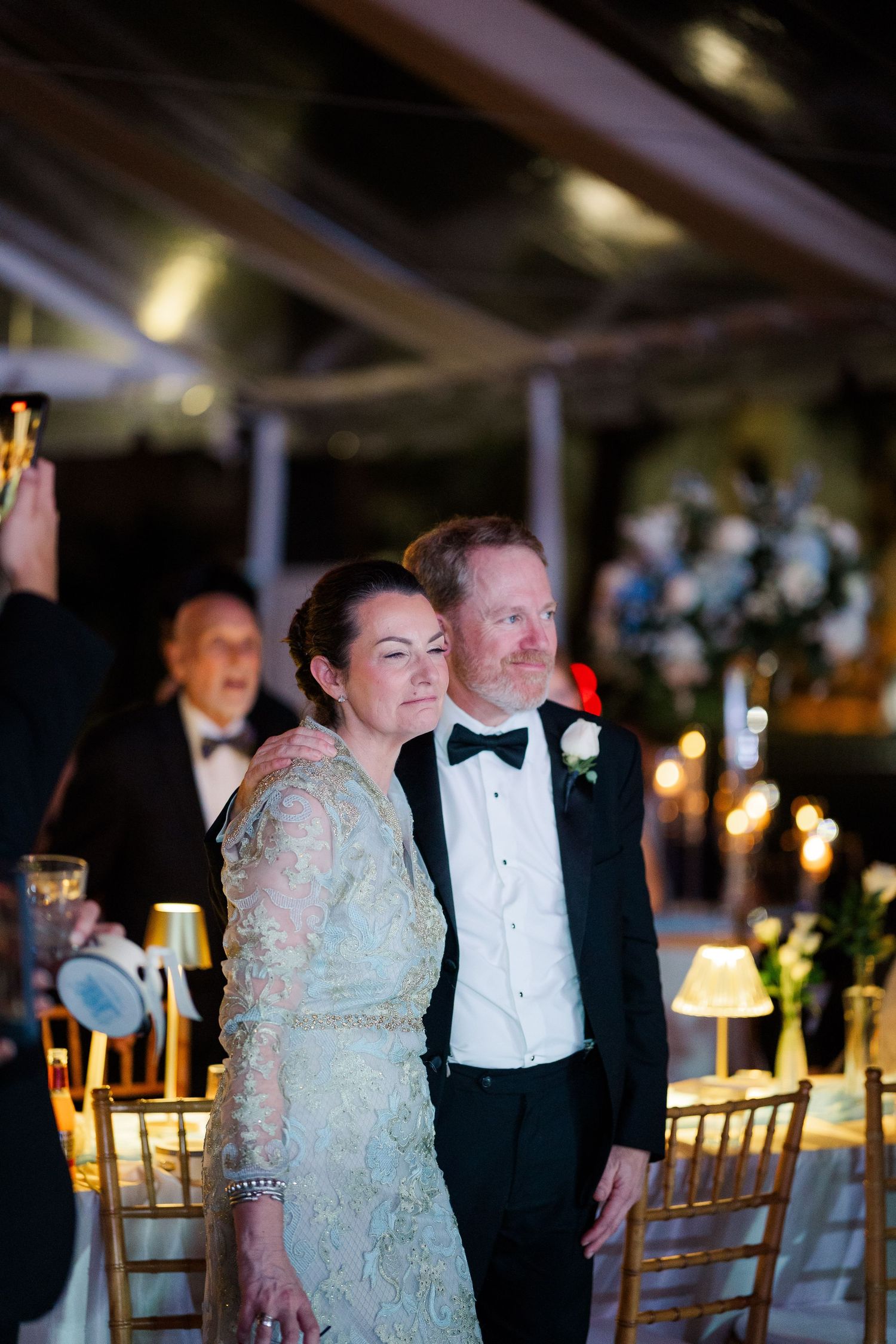 Formal evening wedding reception with guests in black tie attire seated at decorated tables.