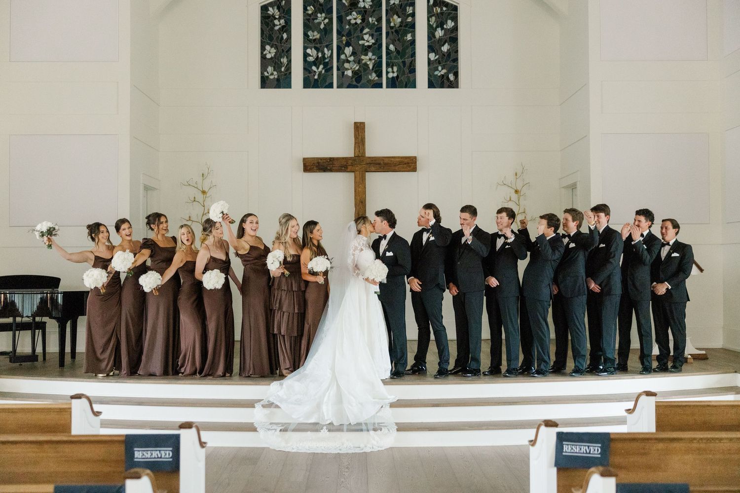 A wedding ceremony setup in a church with brown-clad wedding party members and a prominent cross on display.
