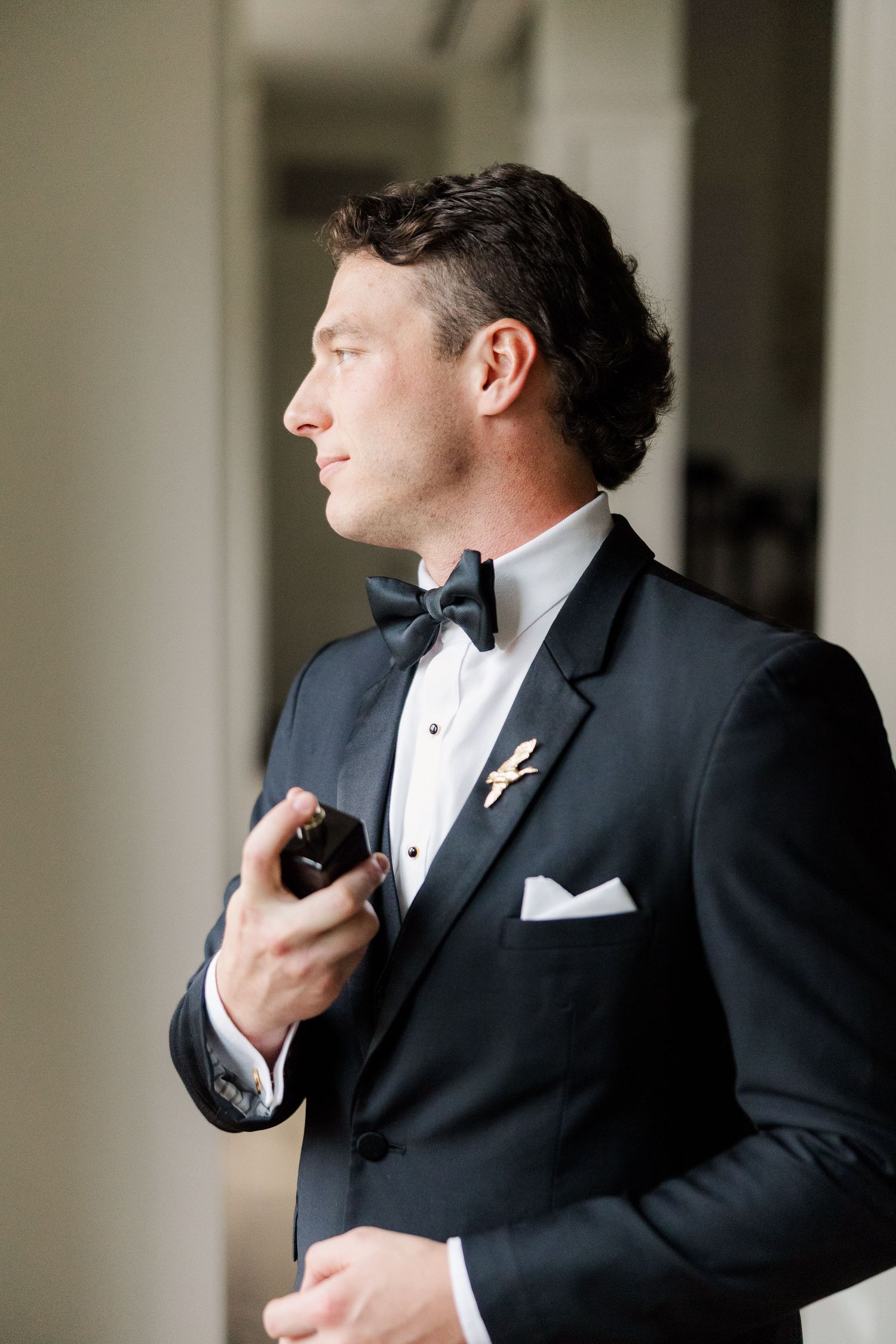 A groom adjusts his bowtie while getting ready in formal attire for a wedding ceremony.