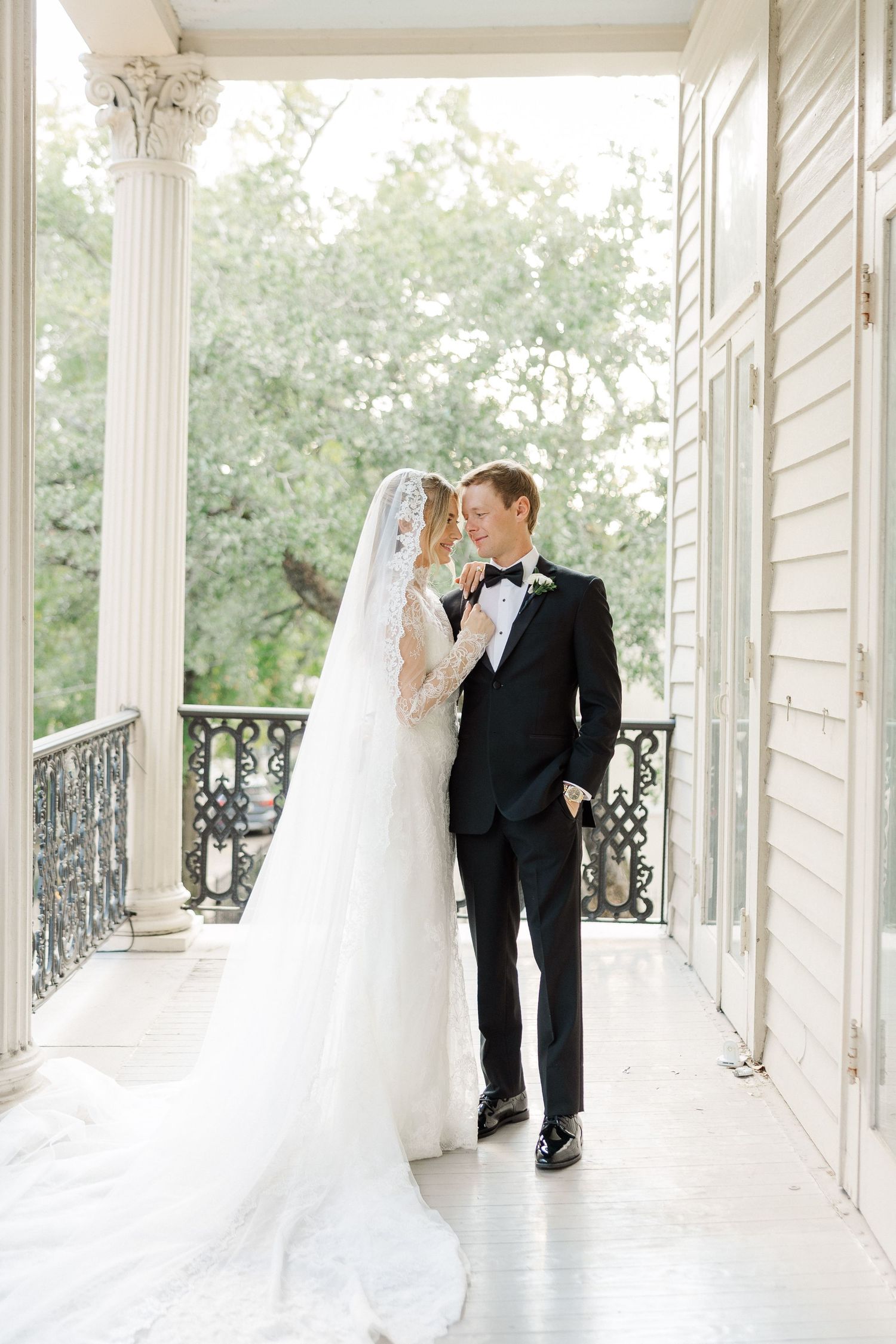 Intimate wedding moment captured on white columned porch with natural lighting.