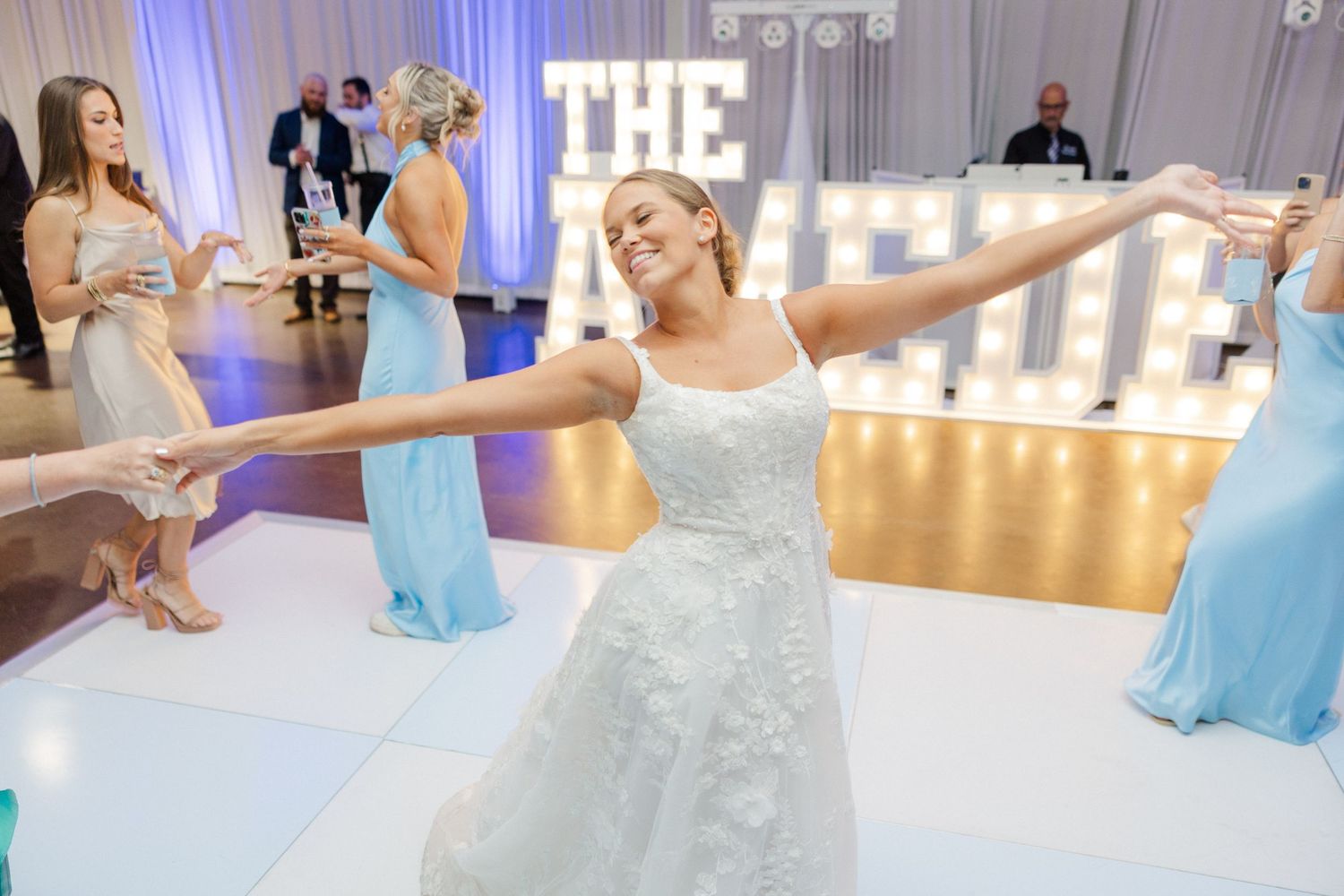 Wedding guests dance and celebrate on the dance floor with bridesmaids in light blue dresses.