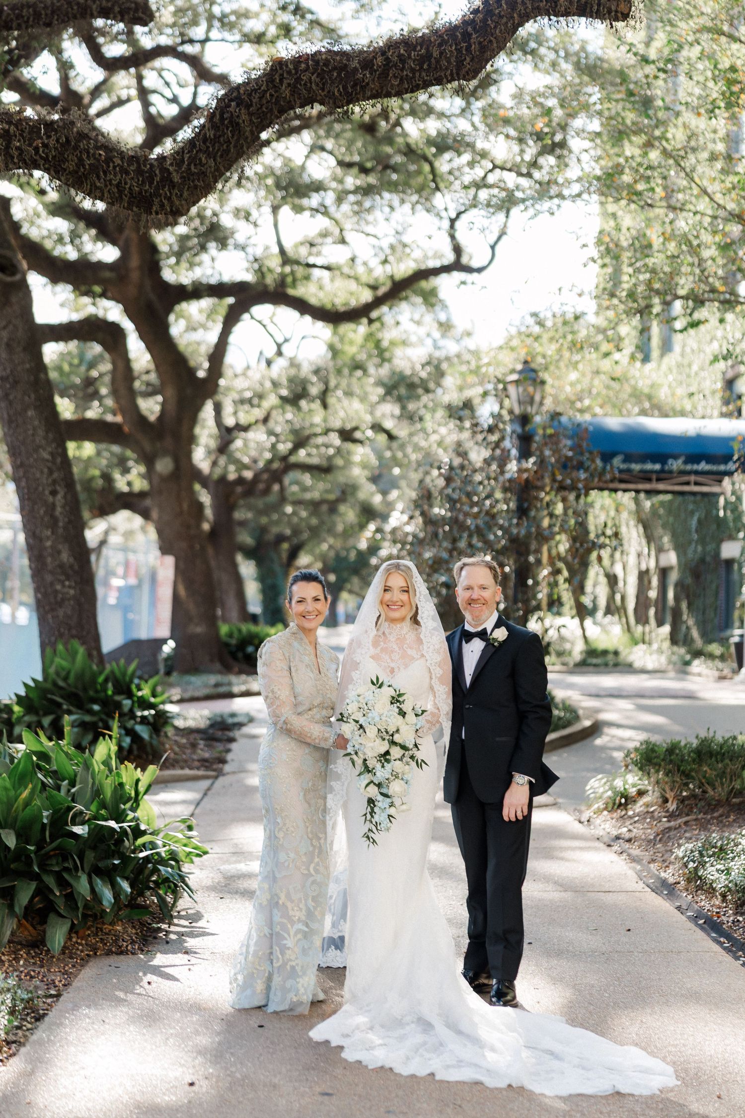 A wedding ceremony under oak trees with a bride in a flowing white gown and cascading bouquet.