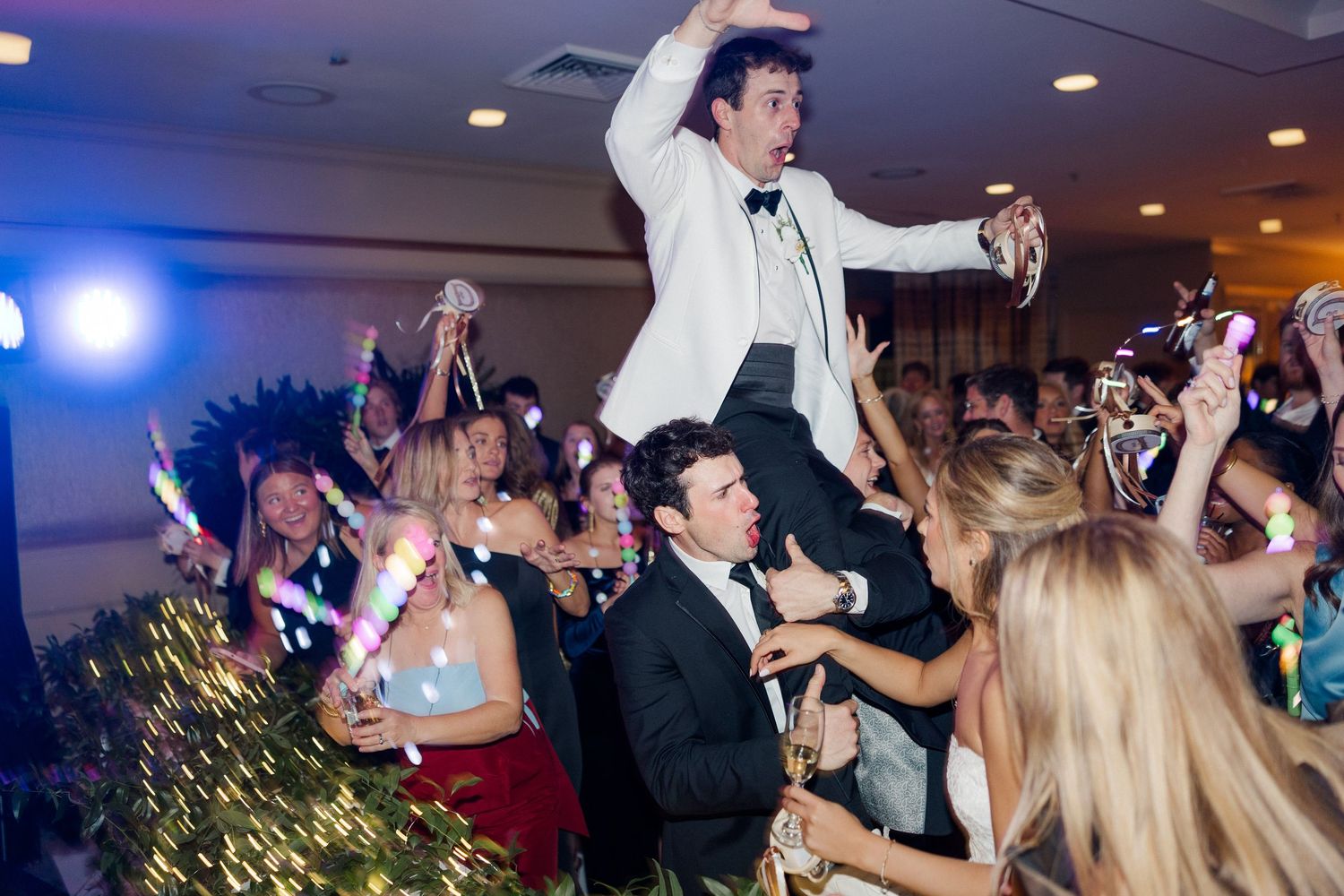 Wedding reception guests lift and celebrate during an energetic dance party moment.