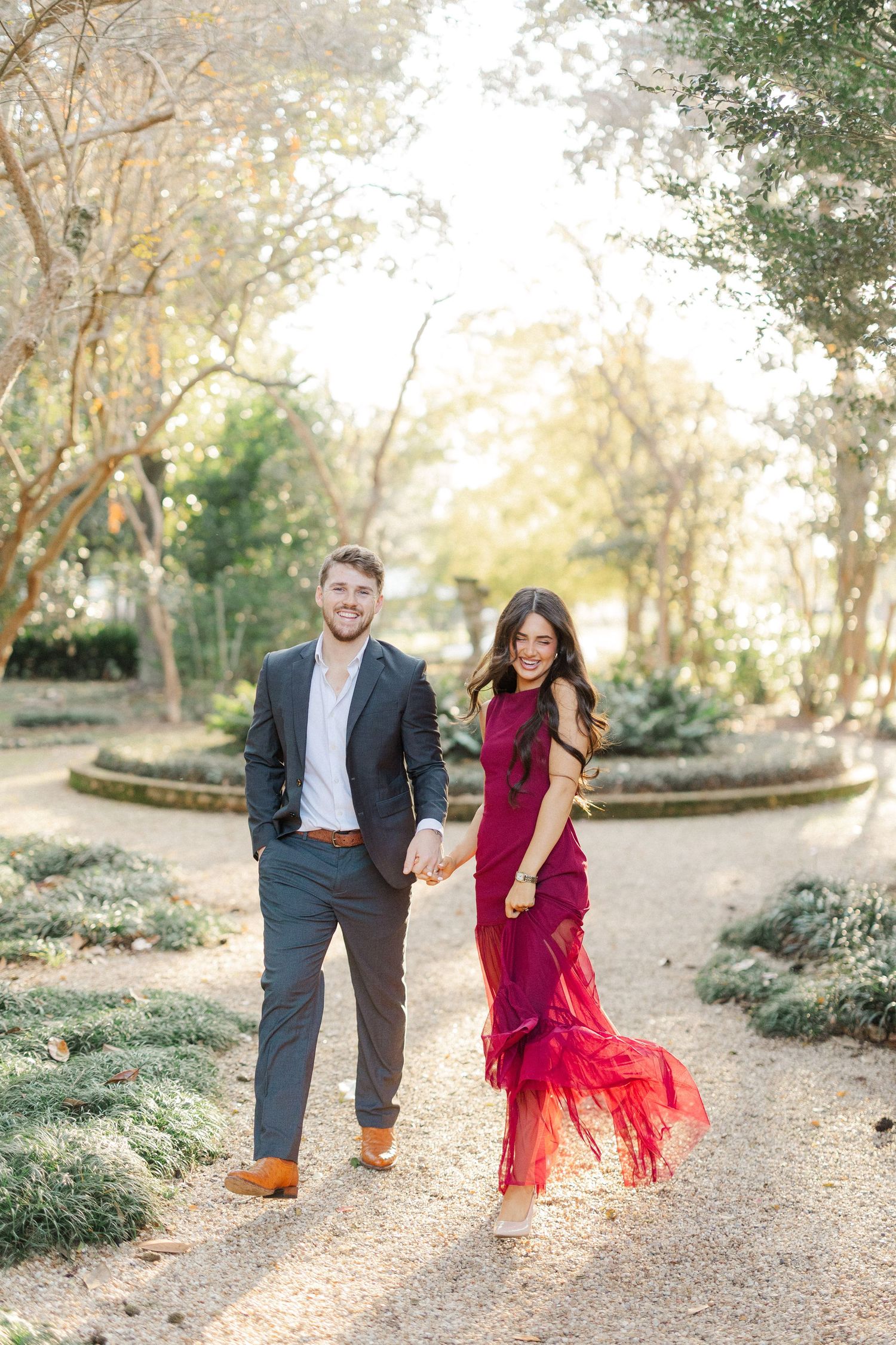 A playful couple runs together on a garden path during their engagement photo session.