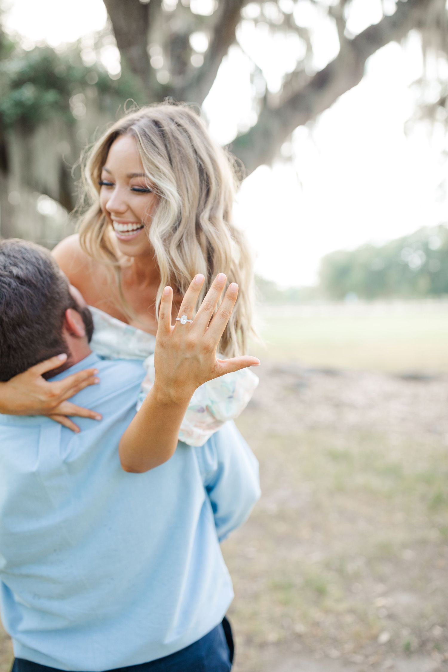 A joyful moment captured outdoors showing genuine laughter and a sparkling engagement ring.
