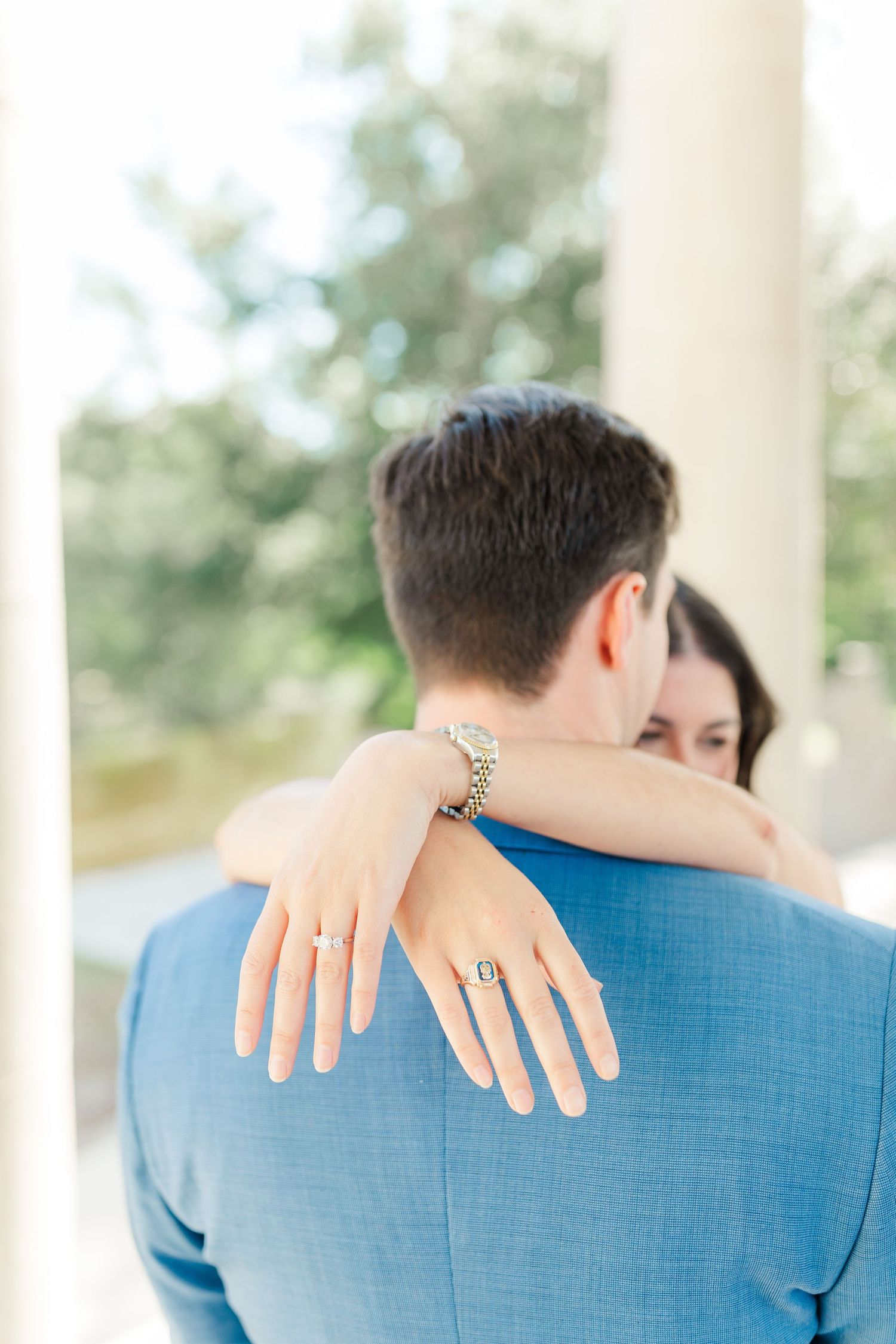 Couple embracing while showing off engagement ring with arms around each other in romantic outdoor setting.