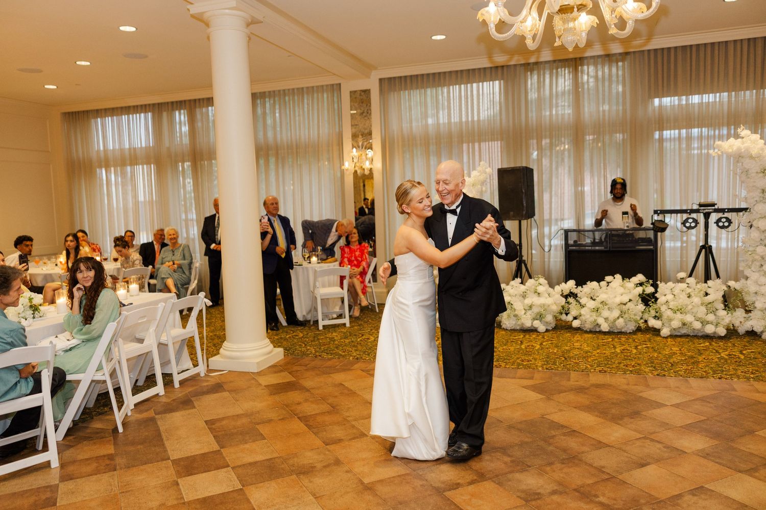 A panoramic view of an elegant wedding reception hall with white decor, chandeliers and dance floor.