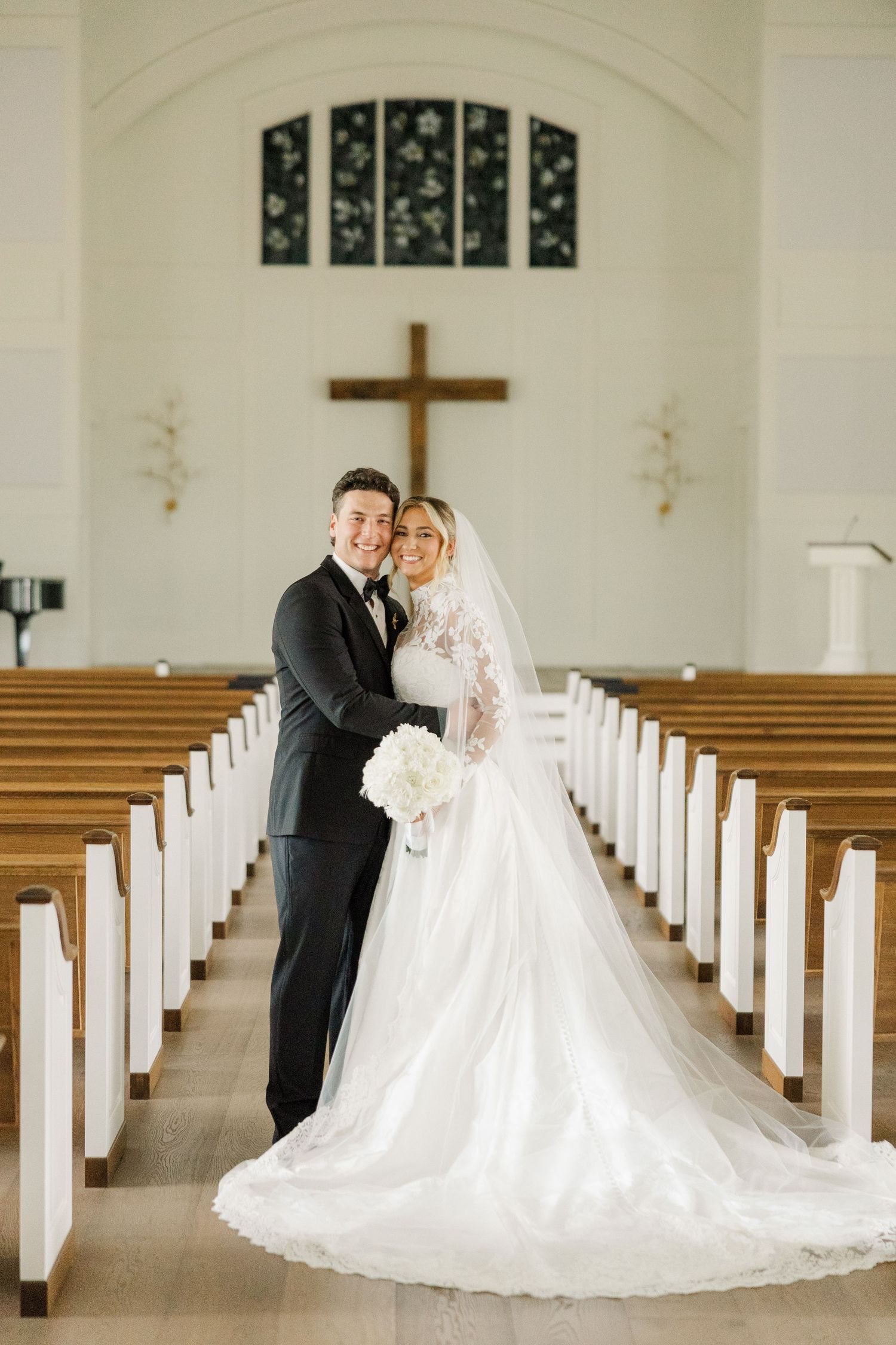 A couple embraces during their wedding ceremony in a bright church sanctuary with wooden pews.