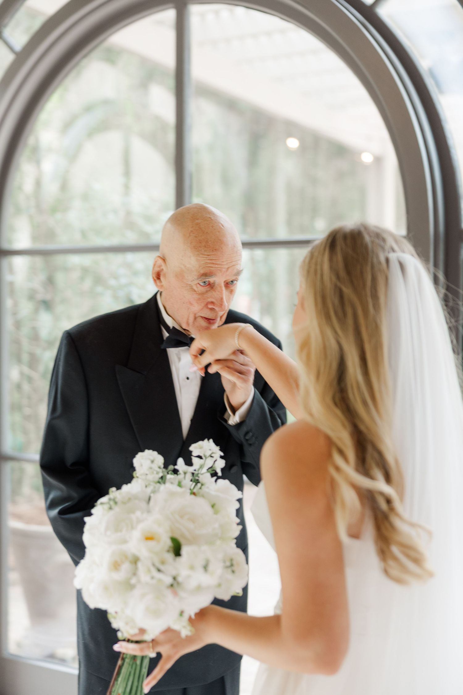 Emotional first look between a bride in white and an older man in formal attire during a wedding ceremony.