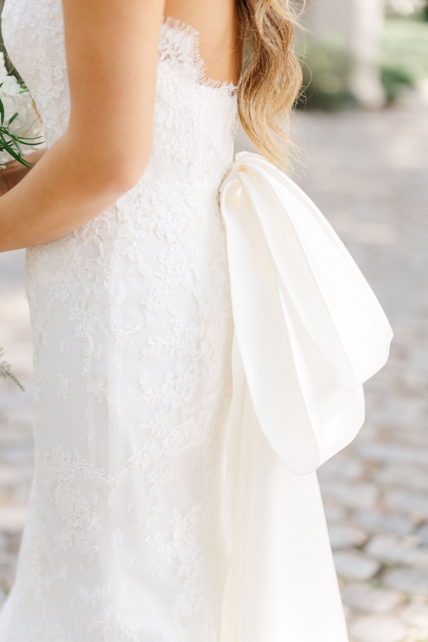 Close-up details of an elegant white lace wedding dress with a large bow accent.