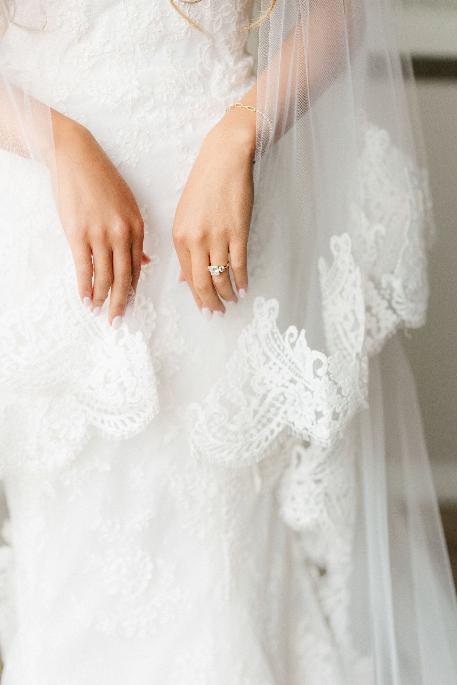 Close-up detail of delicate white lace trim on a wedding dress with a sparkling engagement ring.