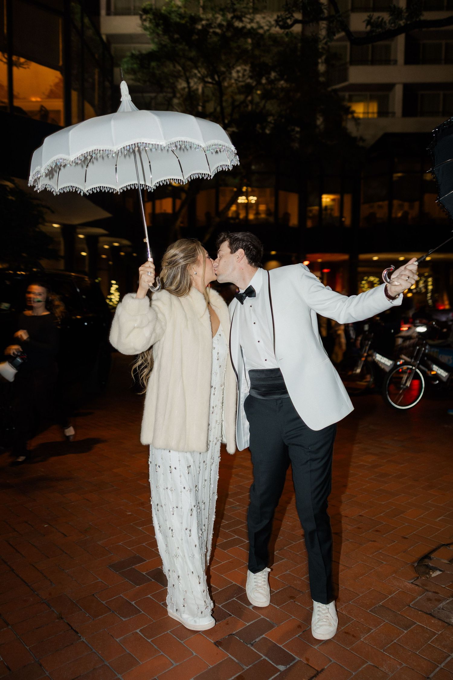 Couple posing with a decorative white umbrella at night on brick pavement.
