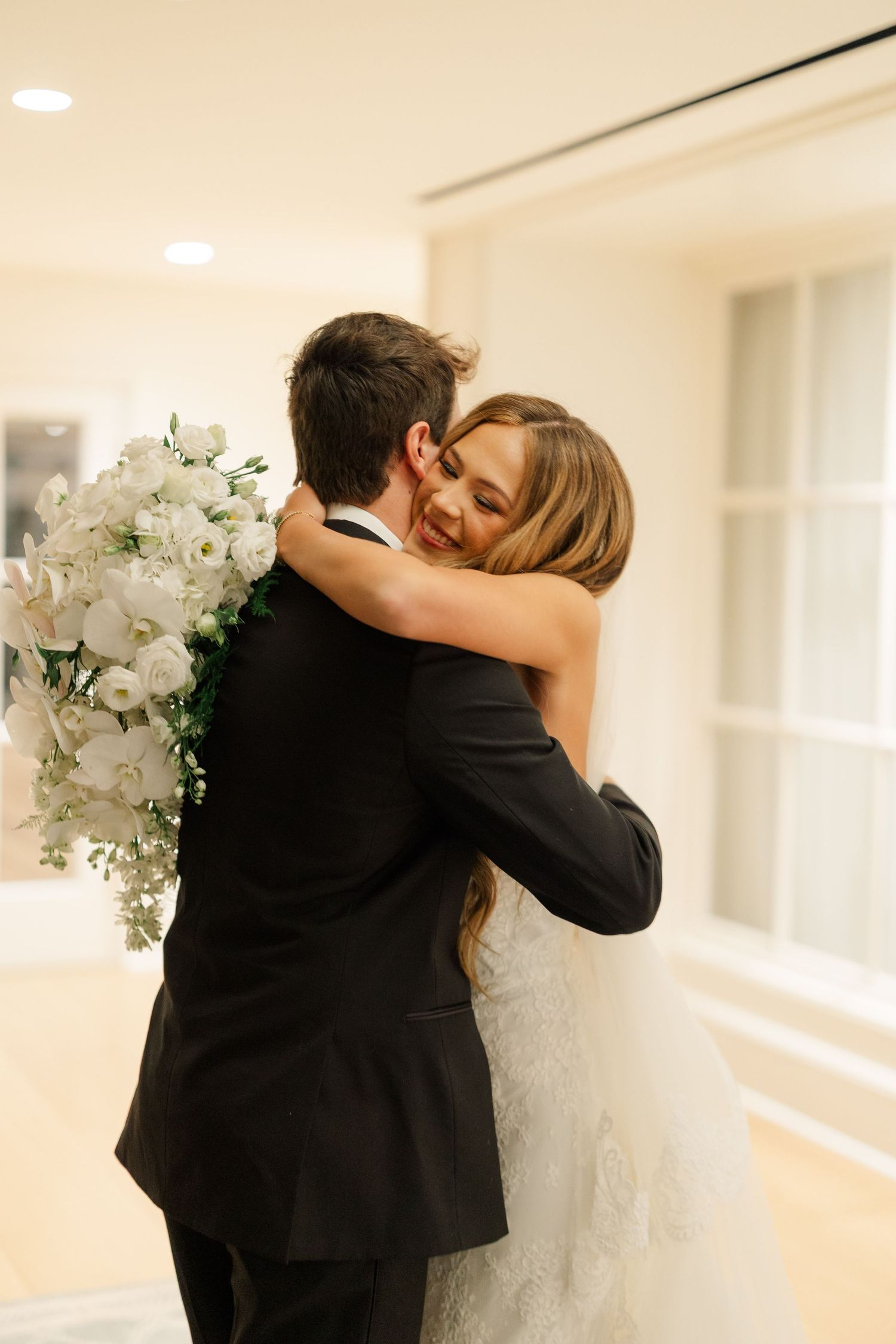 Wedding couple embracing in a bright hallway decorated with white orchids.