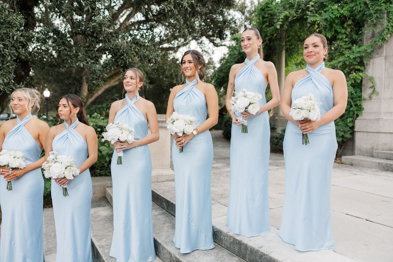 Row of bridesmaids in matching pale blue dresses holding white floral bouquets.